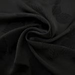 Detailed black botanical leaf print viscose fabric showing woven texture