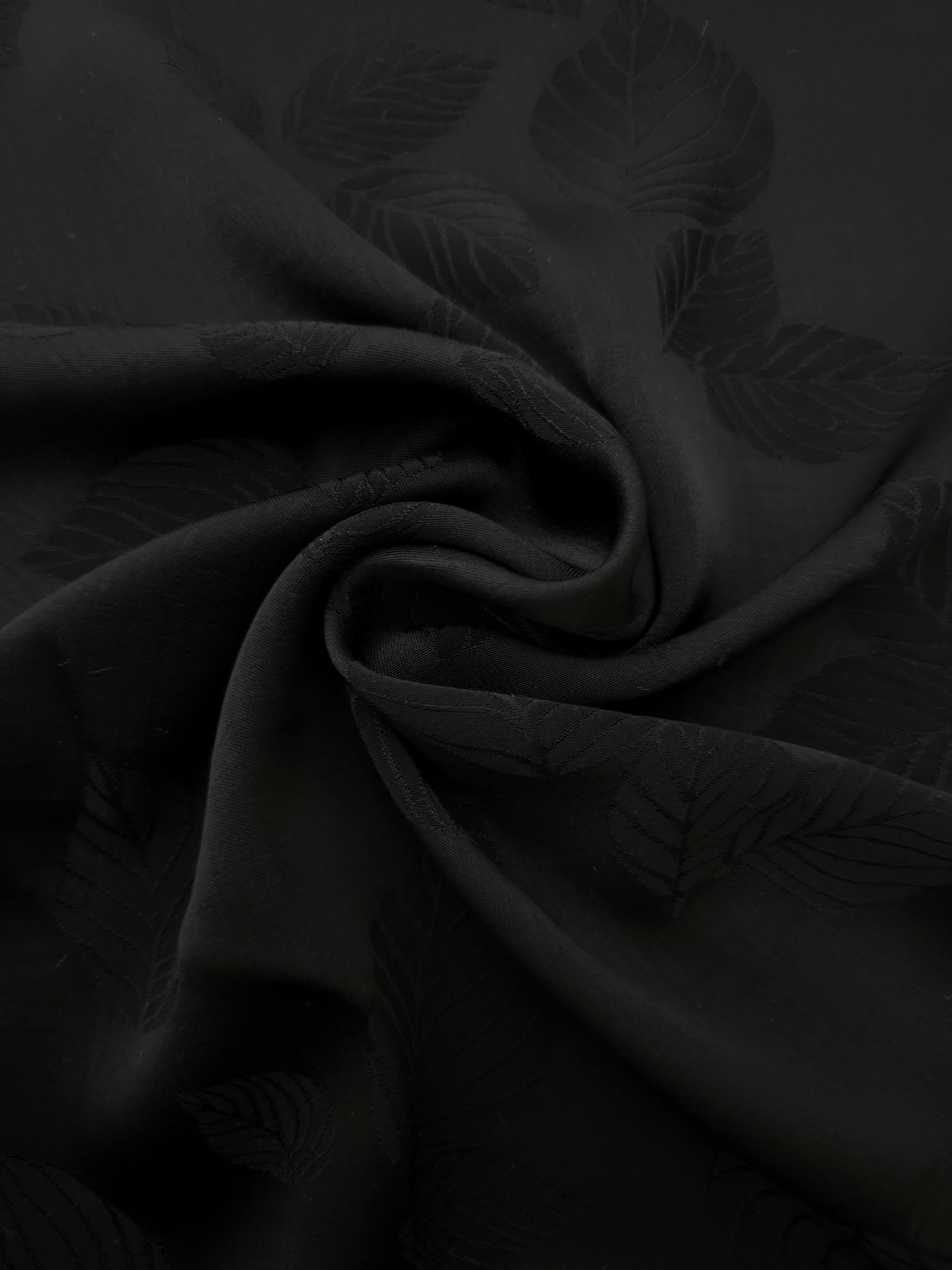 Detailed black botanical leaf print viscose fabric showing woven texture