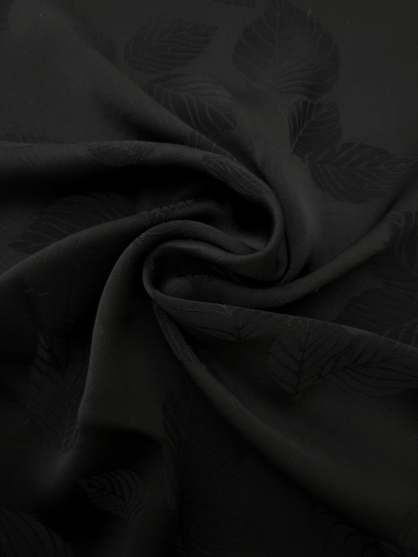 Detailed black botanical leaf print viscose fabric showing woven texture