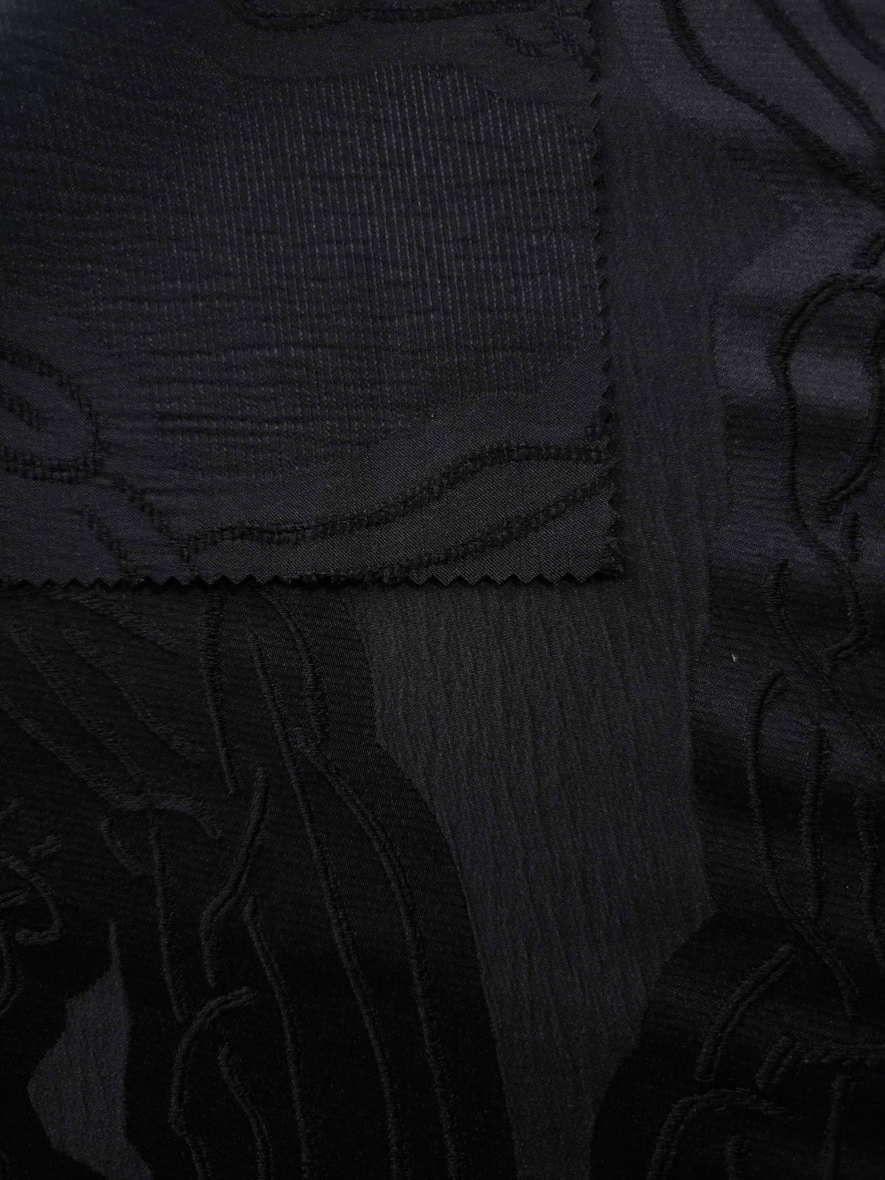 Closeup texture of black laurel polyester crepe jacquard fabric for structured dress layers.