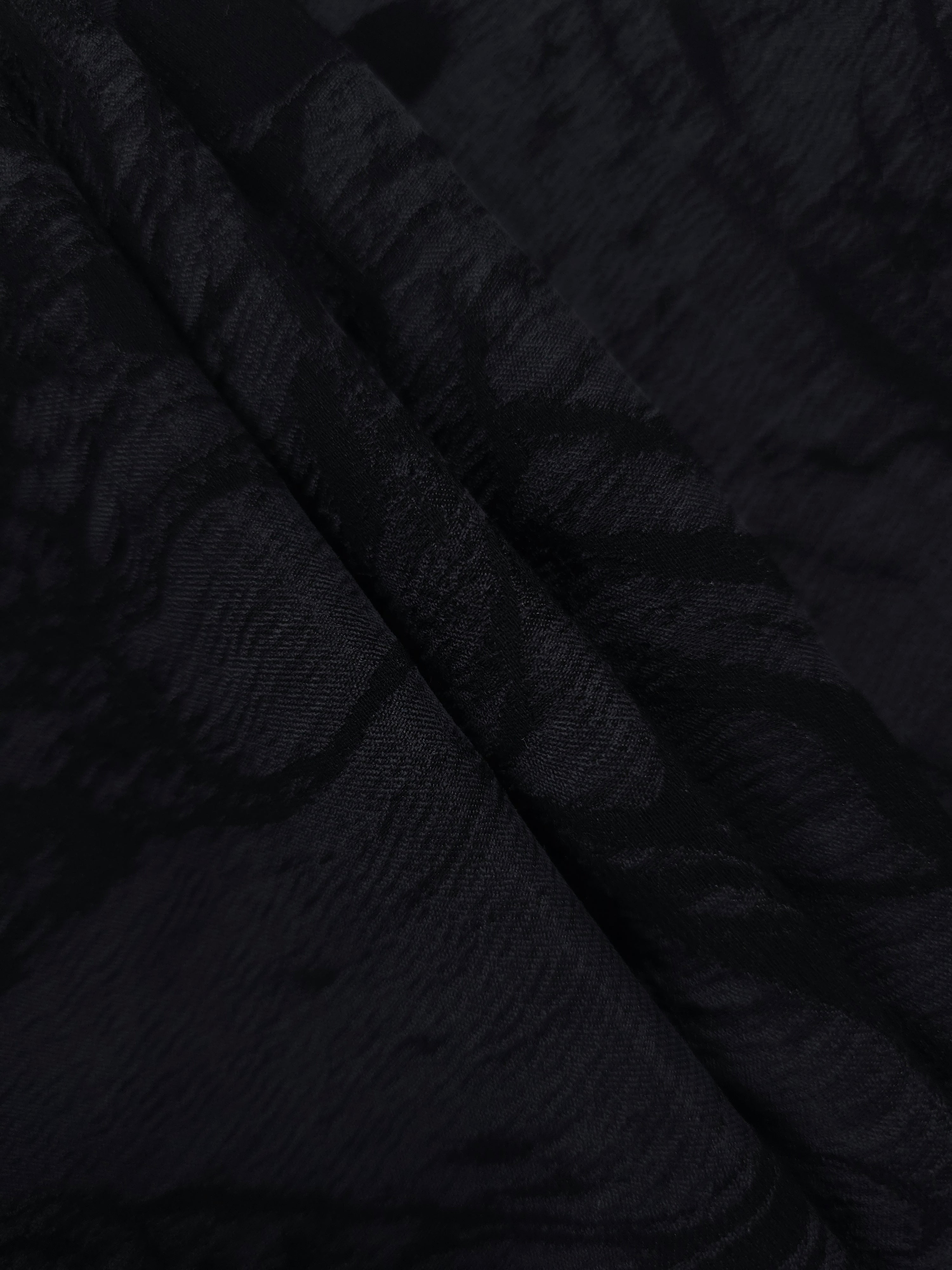 Folded black botanical scroll lyocell viscose jacquard for layered garment sewing.