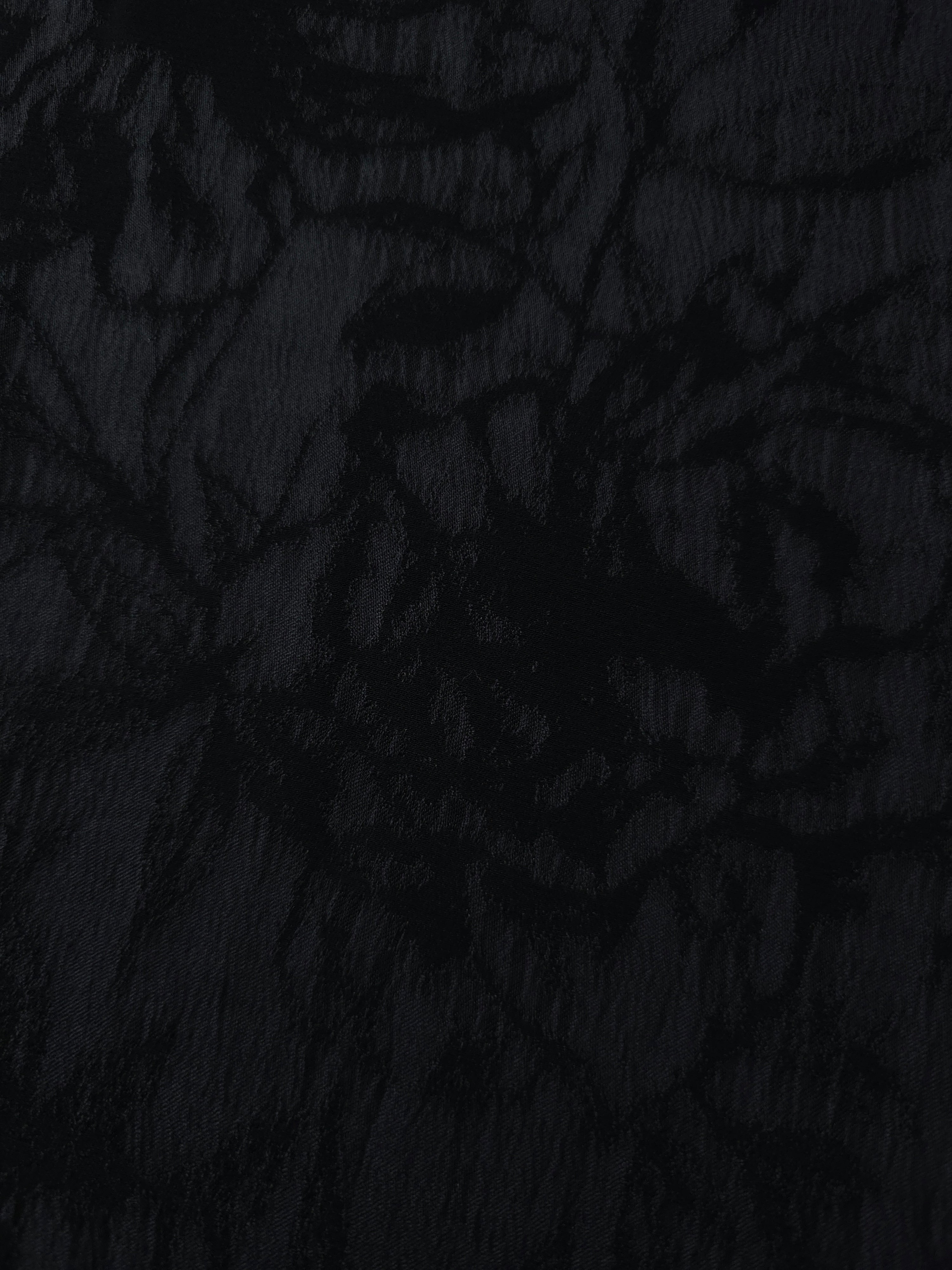 Close texture of black floral vine jacquard showing darker raised pattern on smooth base.
