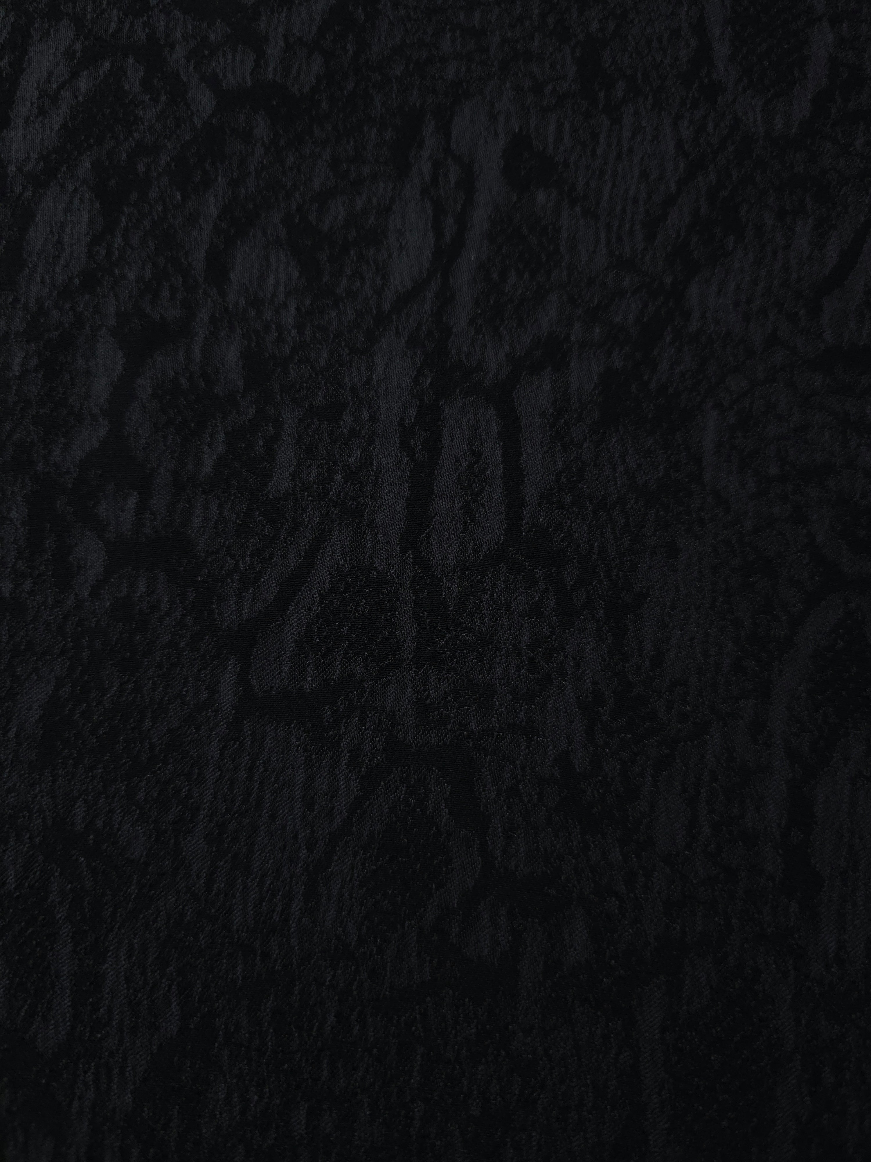 Close texture of black ornamental floral jacquard showing raised woven detail.