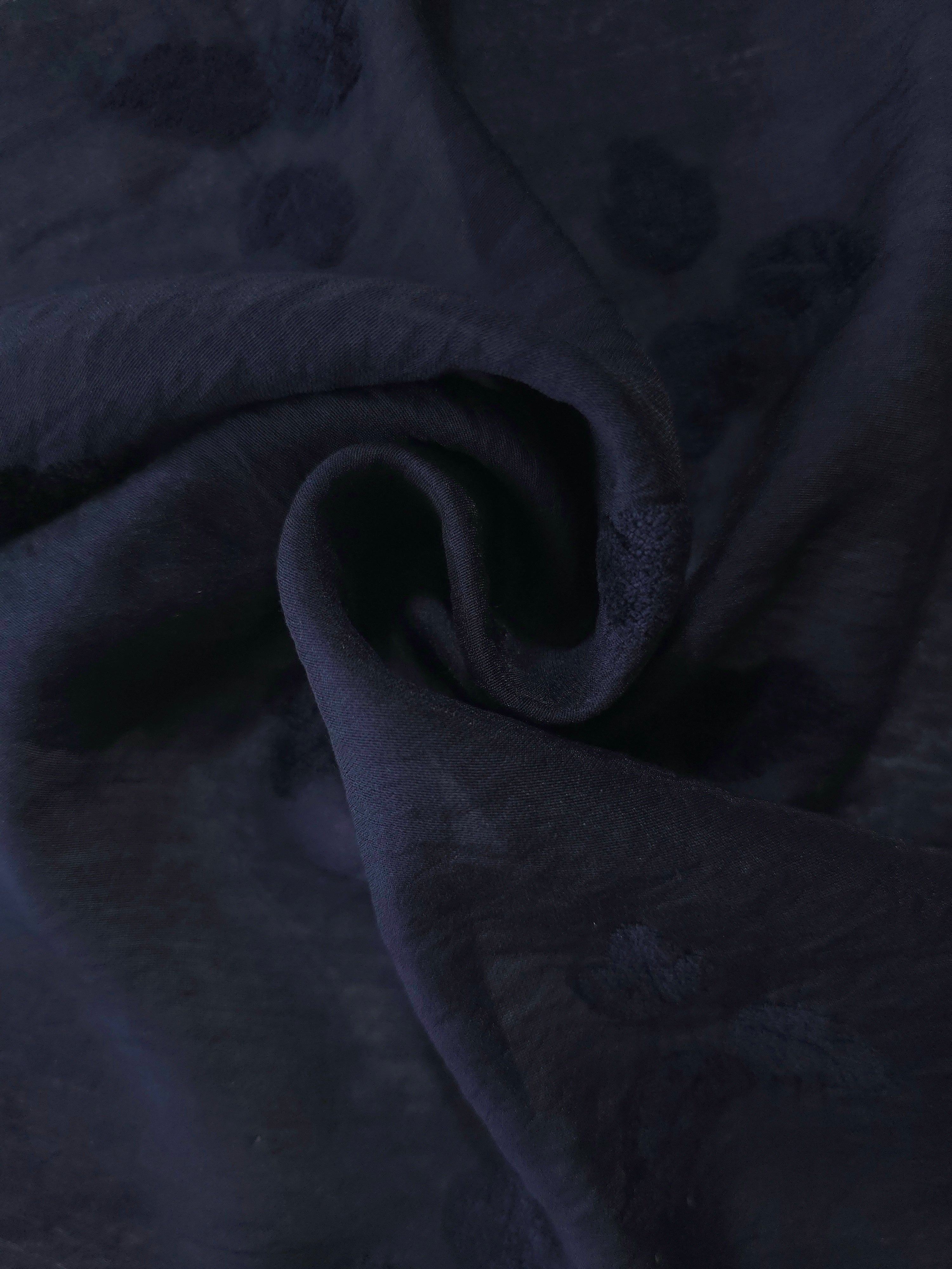 Swirl drape of dark blue small leaf embossed viscose jacquard fabric for kaftan overlays.