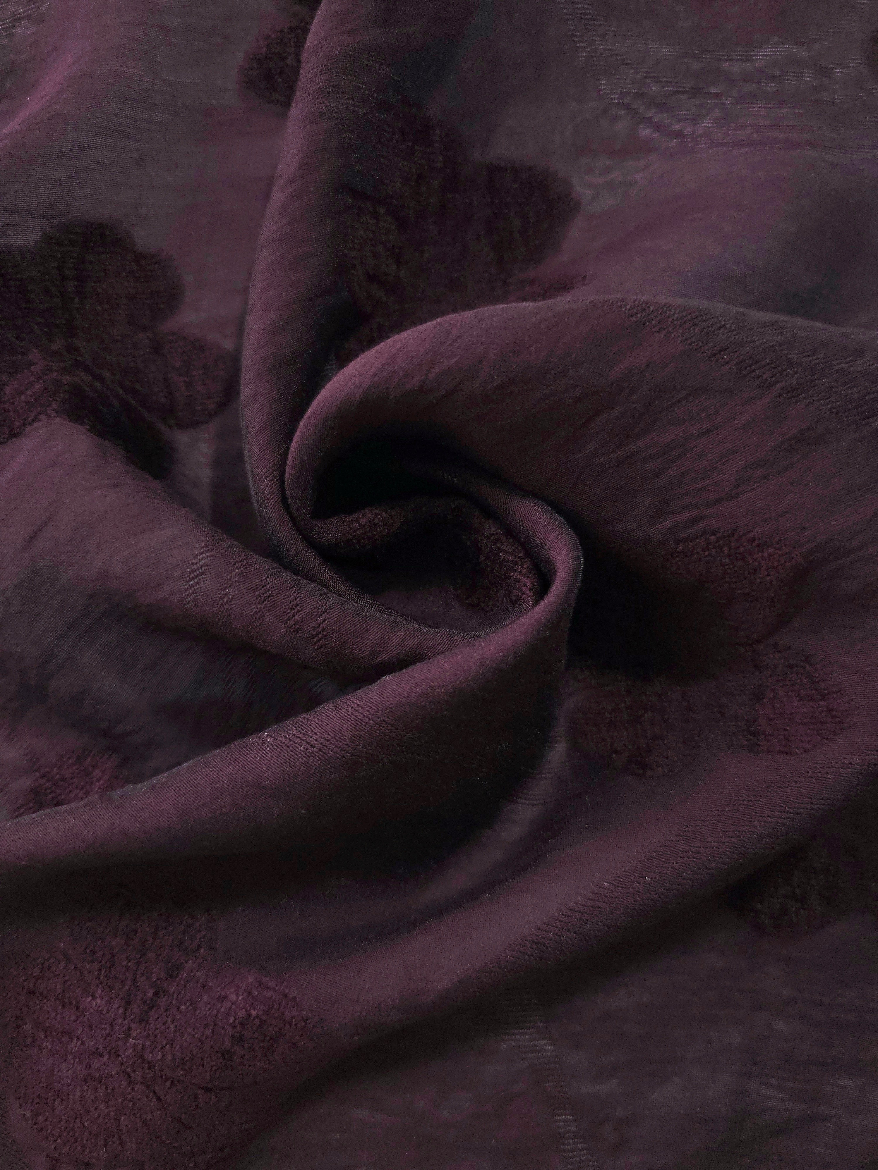 Swirl drape of dark burgundy flower embossed viscose jacquard fabric for overlays.