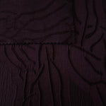 Closeup texture of burgundy laurel polyester crepe jacquard fabric for structured garments.