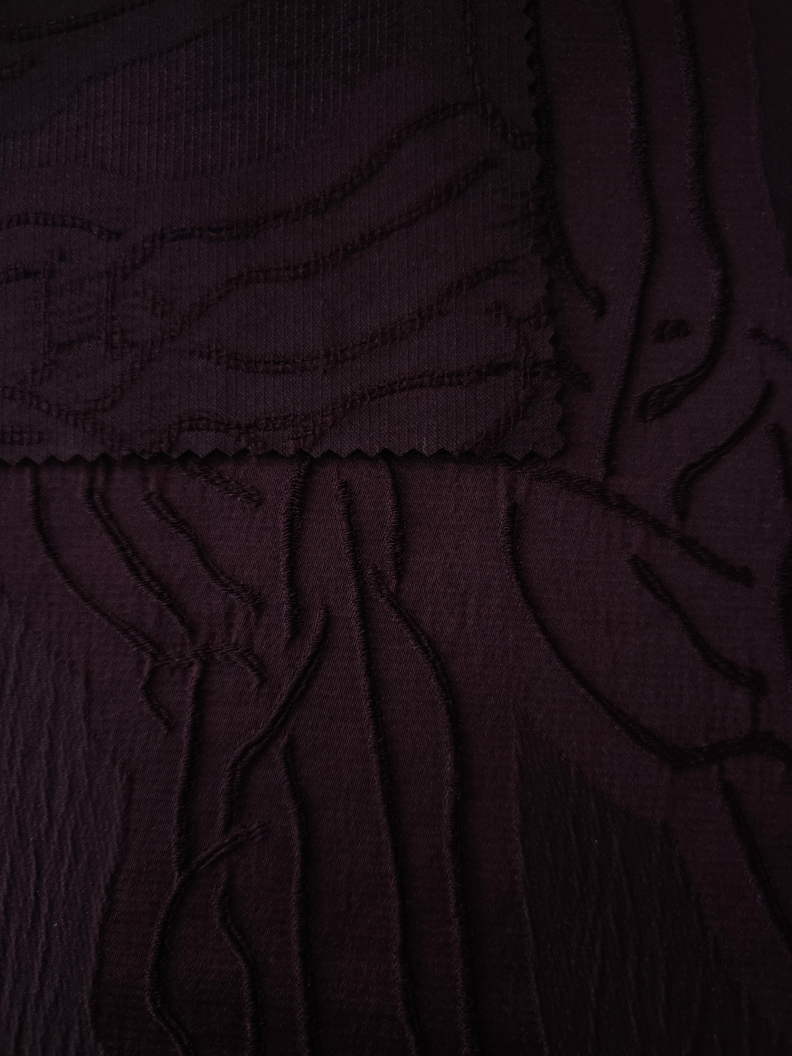 Closeup texture of burgundy laurel polyester crepe jacquard fabric for structured garments.