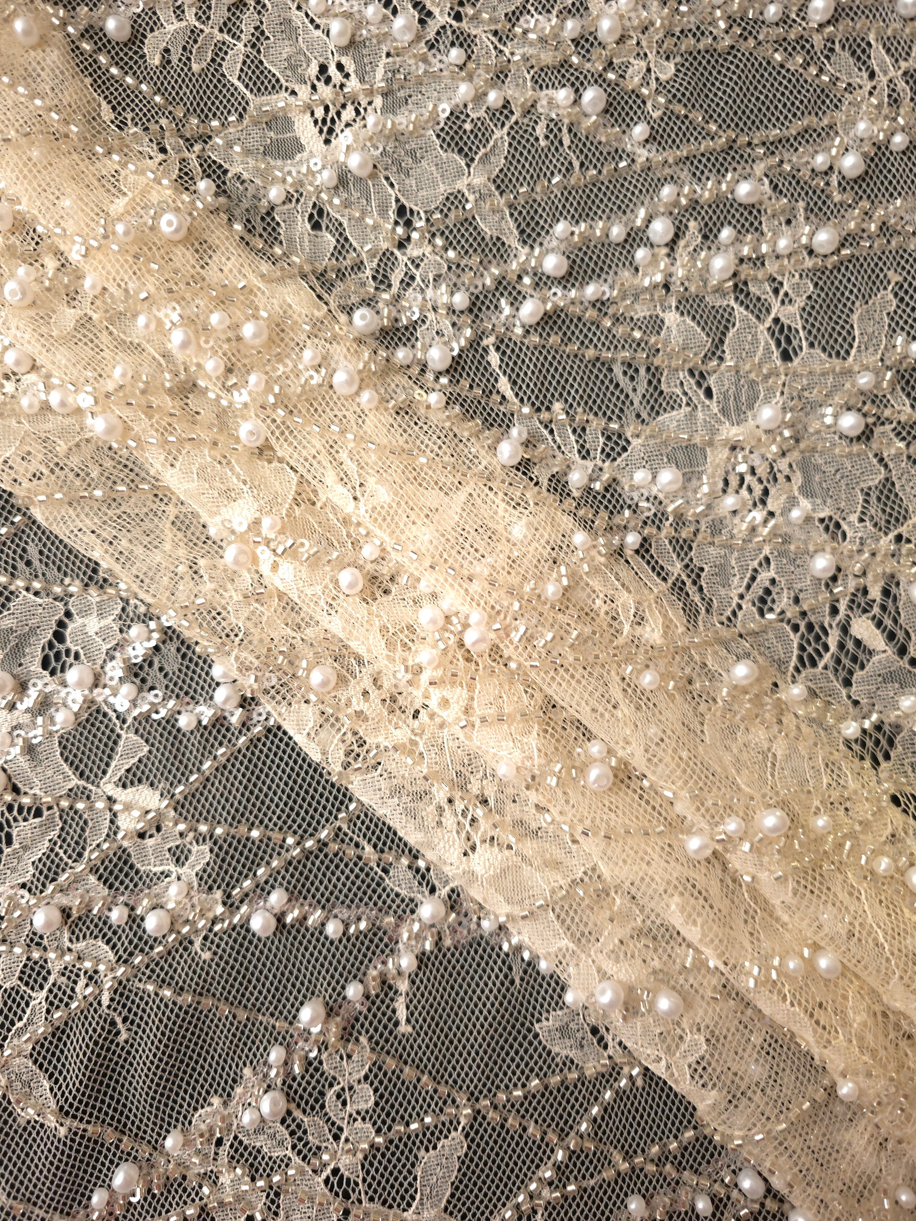 Close-up of Pearl White Botanical Pearl beaded lace showing fine threadwork transparency test, with branching botanical vines with pearl-like beading.