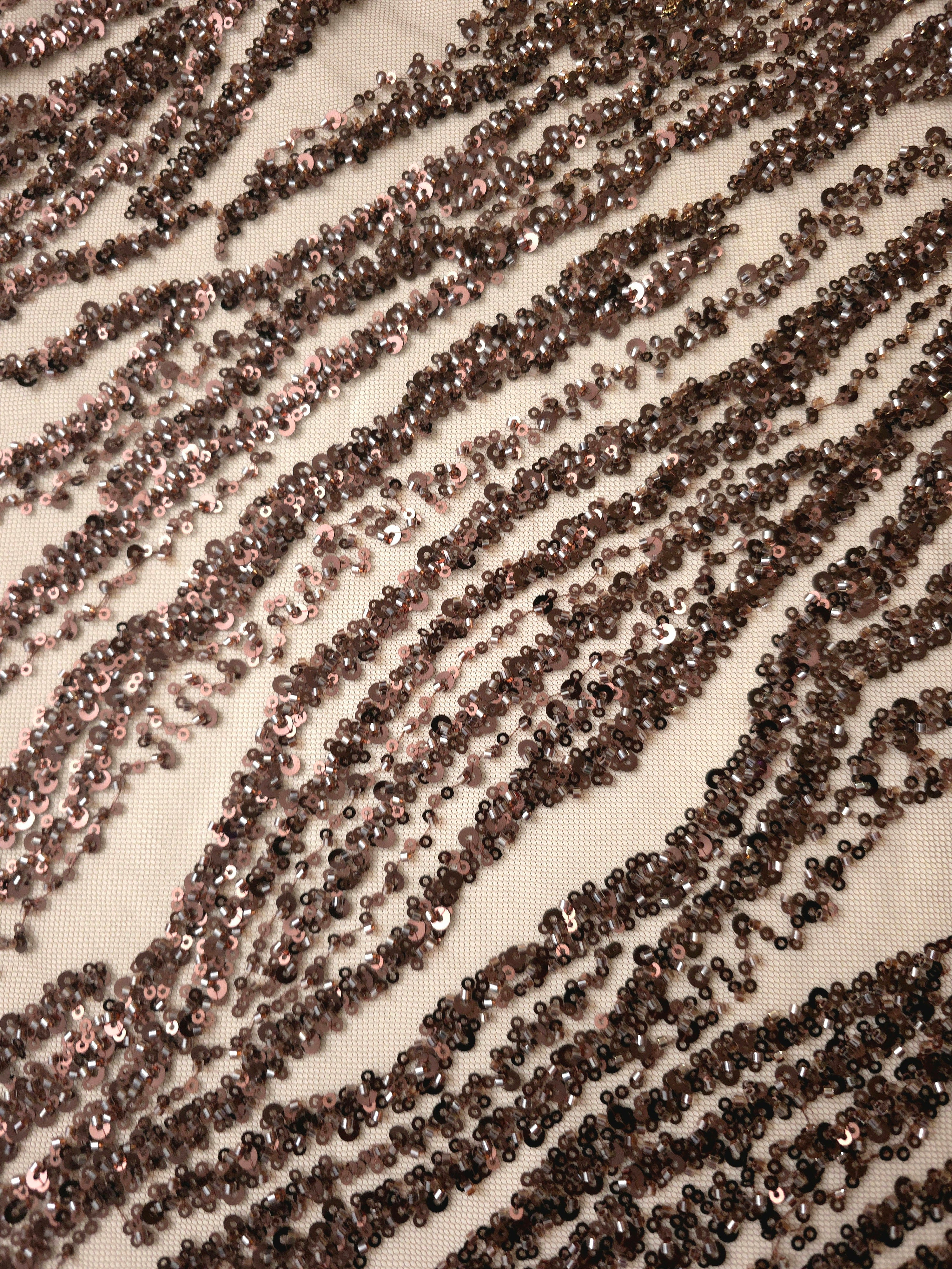 Diagonal close-up of mocha embroidery showing glimmering wave-shaped bands and open mesh spaces.
