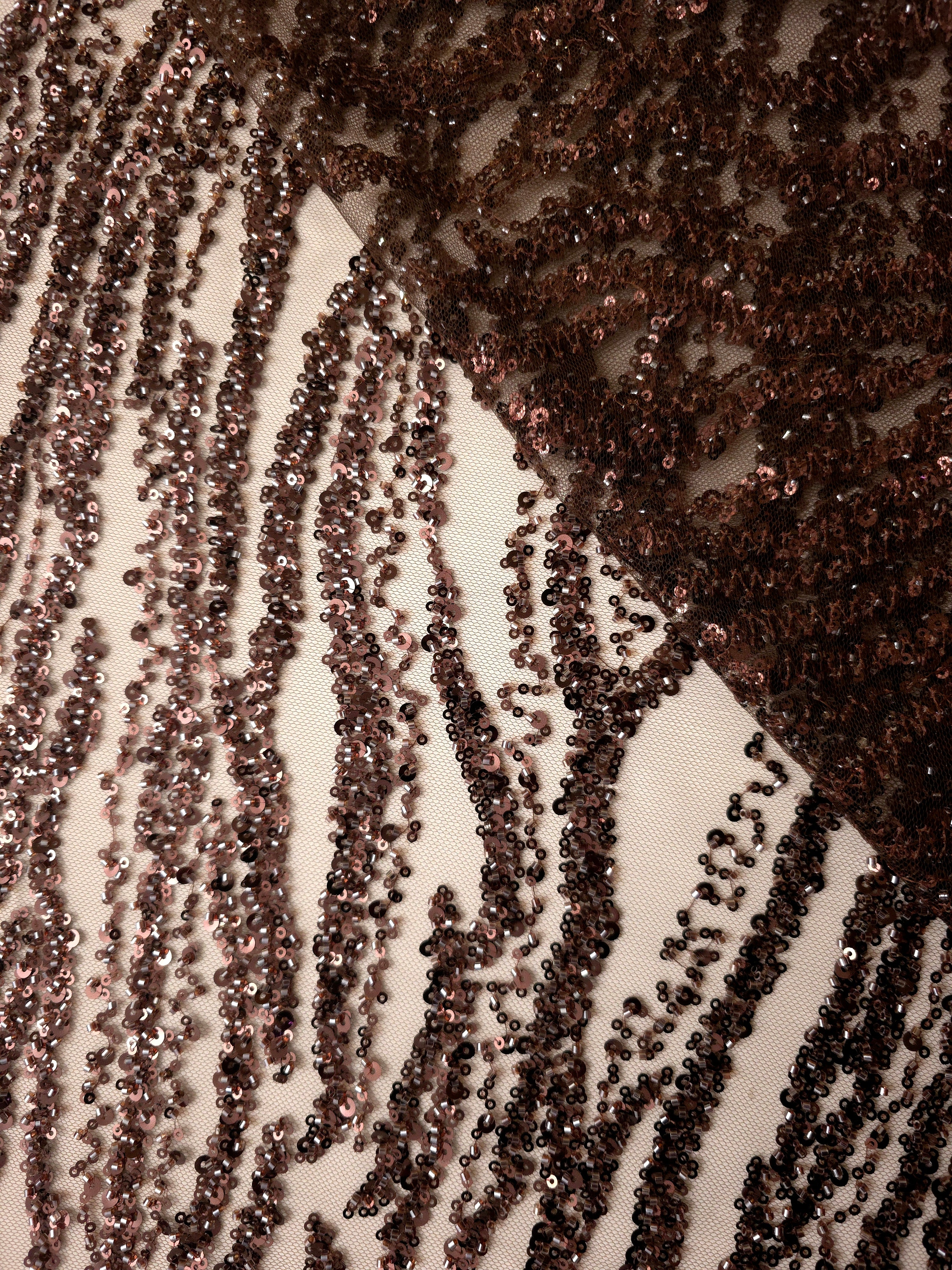 Mocha brown embellished lace folded across itself, contrasting a dense sparkling overlay with sheer patterned fabric.