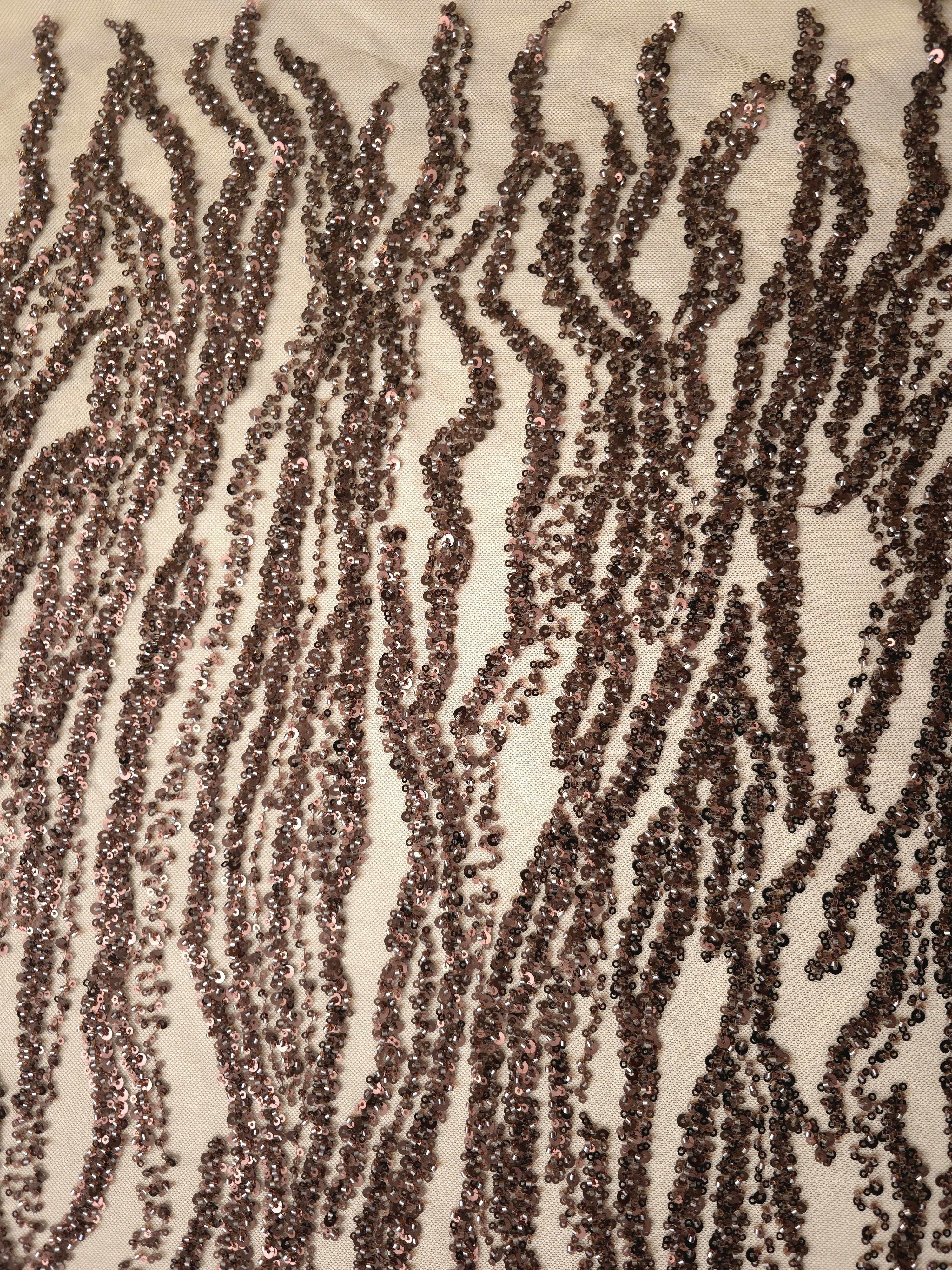 Detailed view of fine brown sequin and bead lines forming irregular ripples on transparent embroidered net.