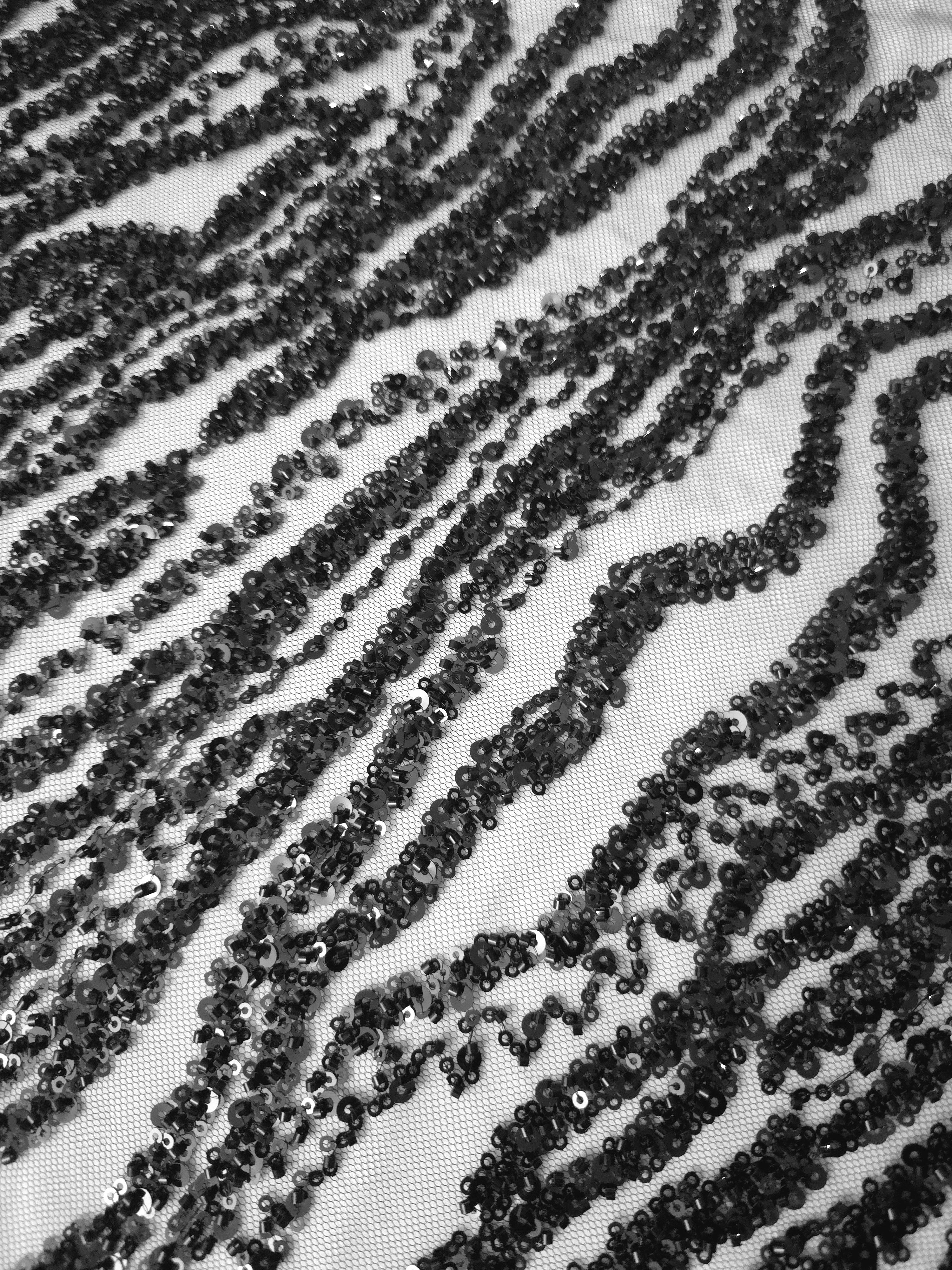 Diagonal photograph of black Zebra Strata embroidery with shimmering dark ripples and visible mesh between lines.