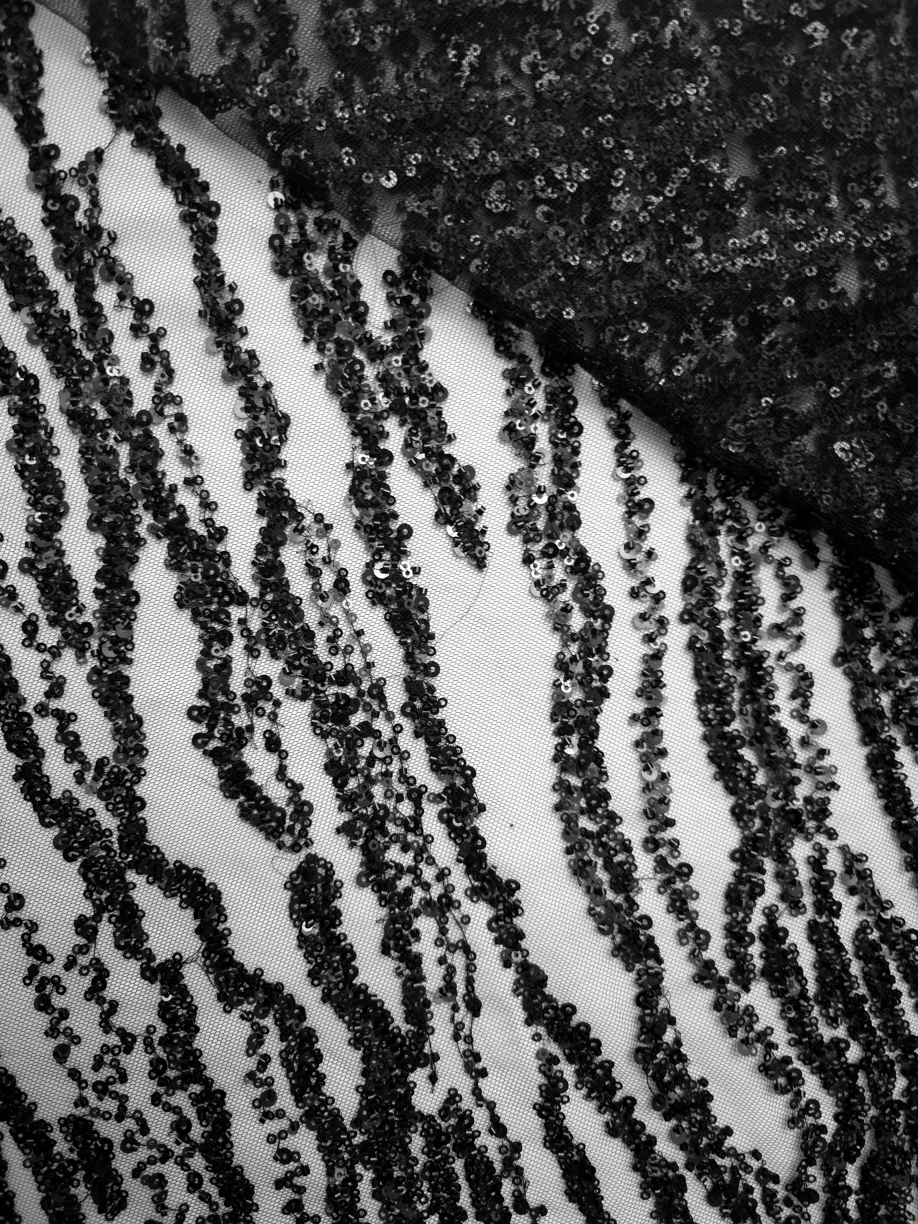 Dark beaded lace detail showing dense onyx embellishment beside open translucent net fabric.