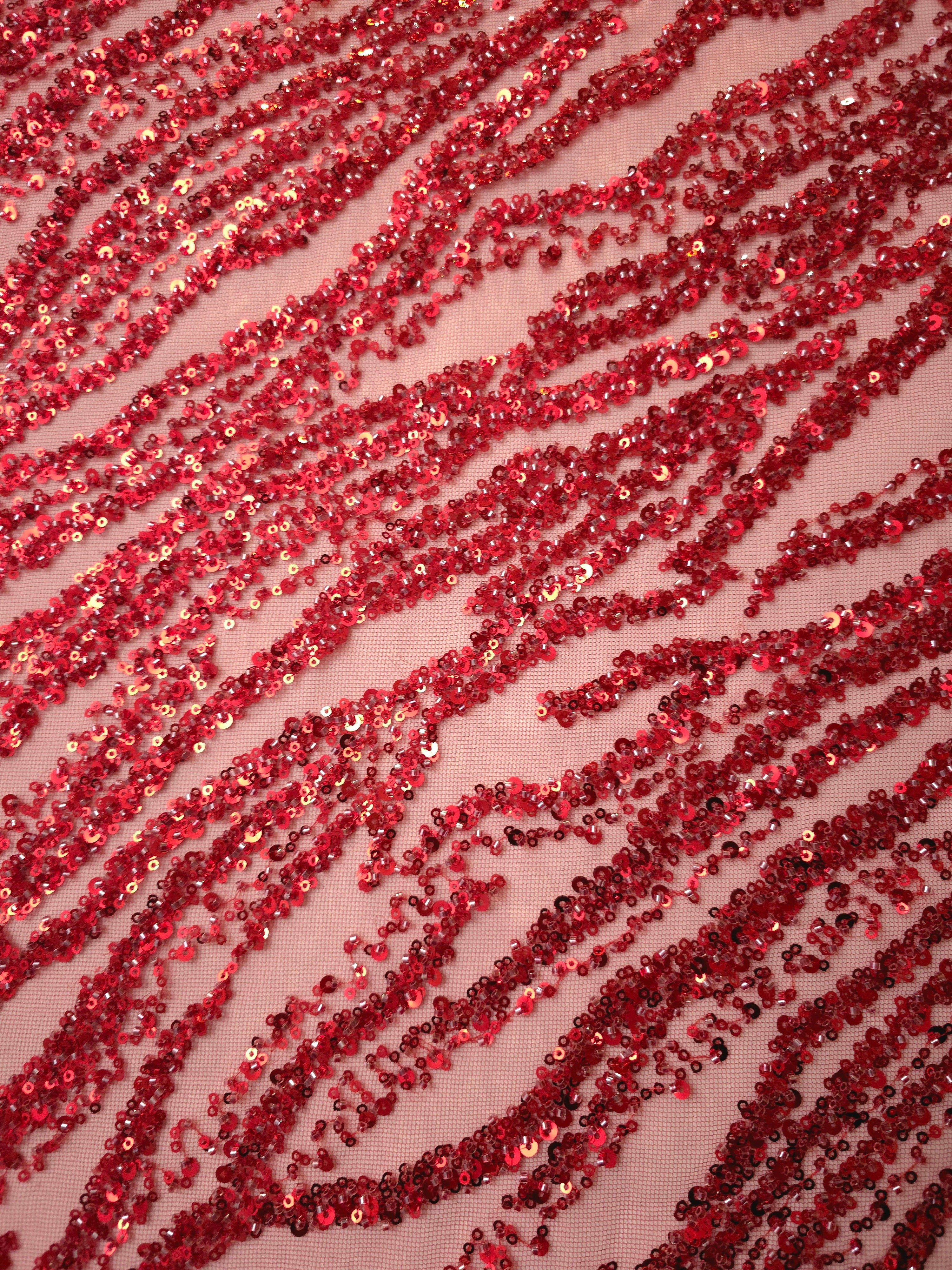 Angled detail of ruby embroidery with curved zebra-inspired bands and glittering raised surface accents.
