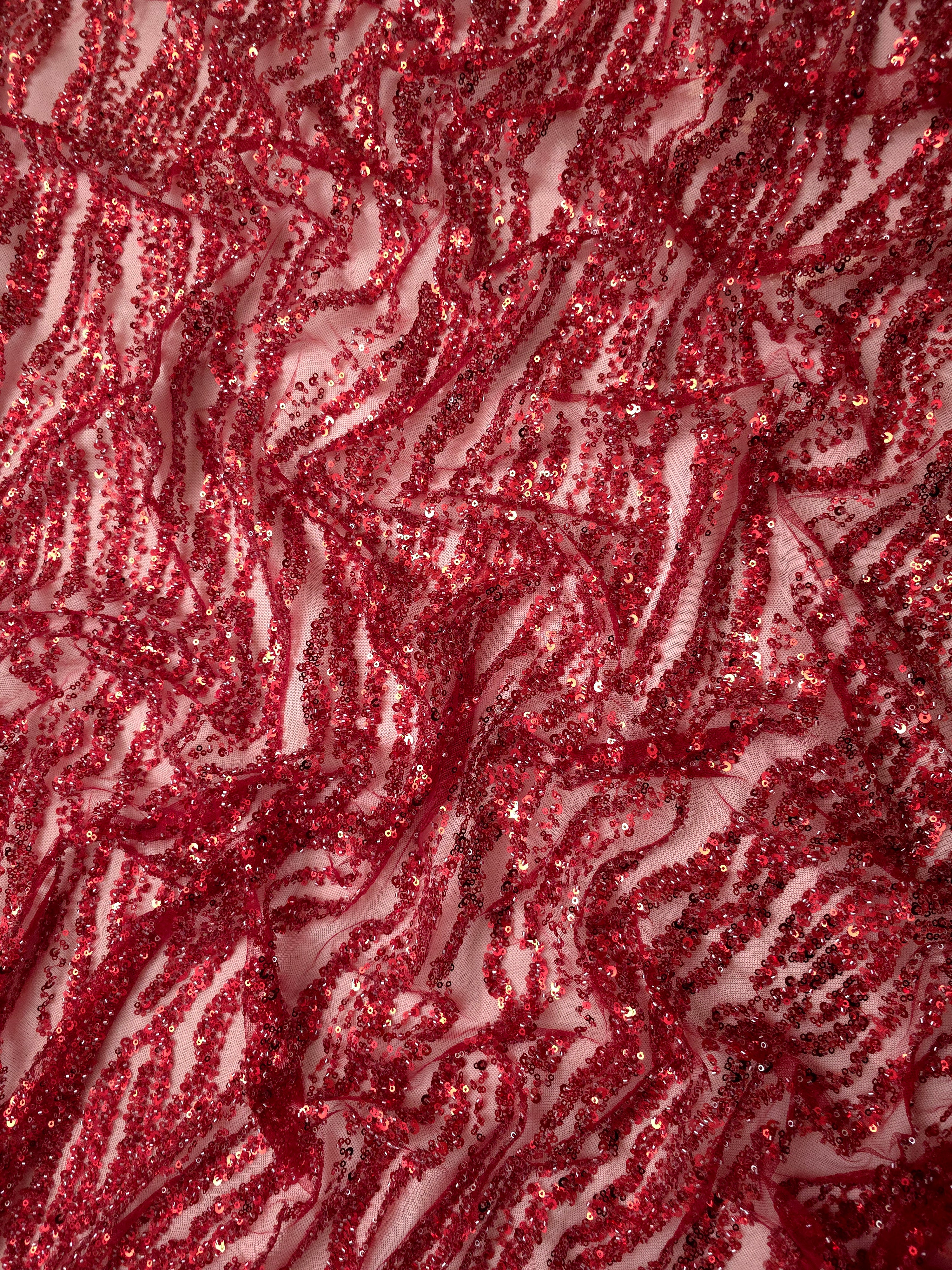 Ruby red embellished fabric draped in soft folds, revealing decorative stripes suited to statement eveningwear.