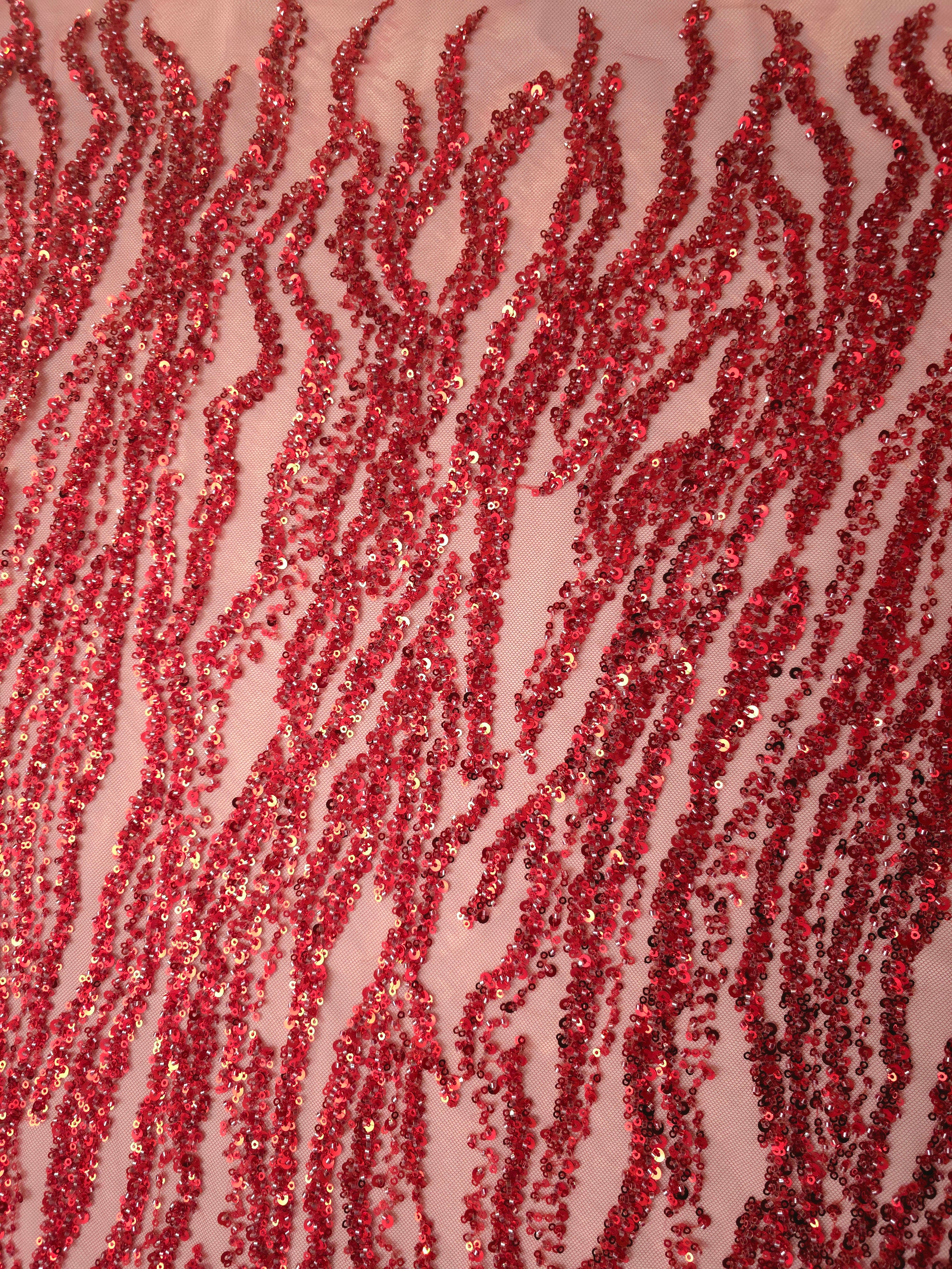 Close-up of sparkling red sequins arranged in irregular ripple motifs on the sheer lace foundation.