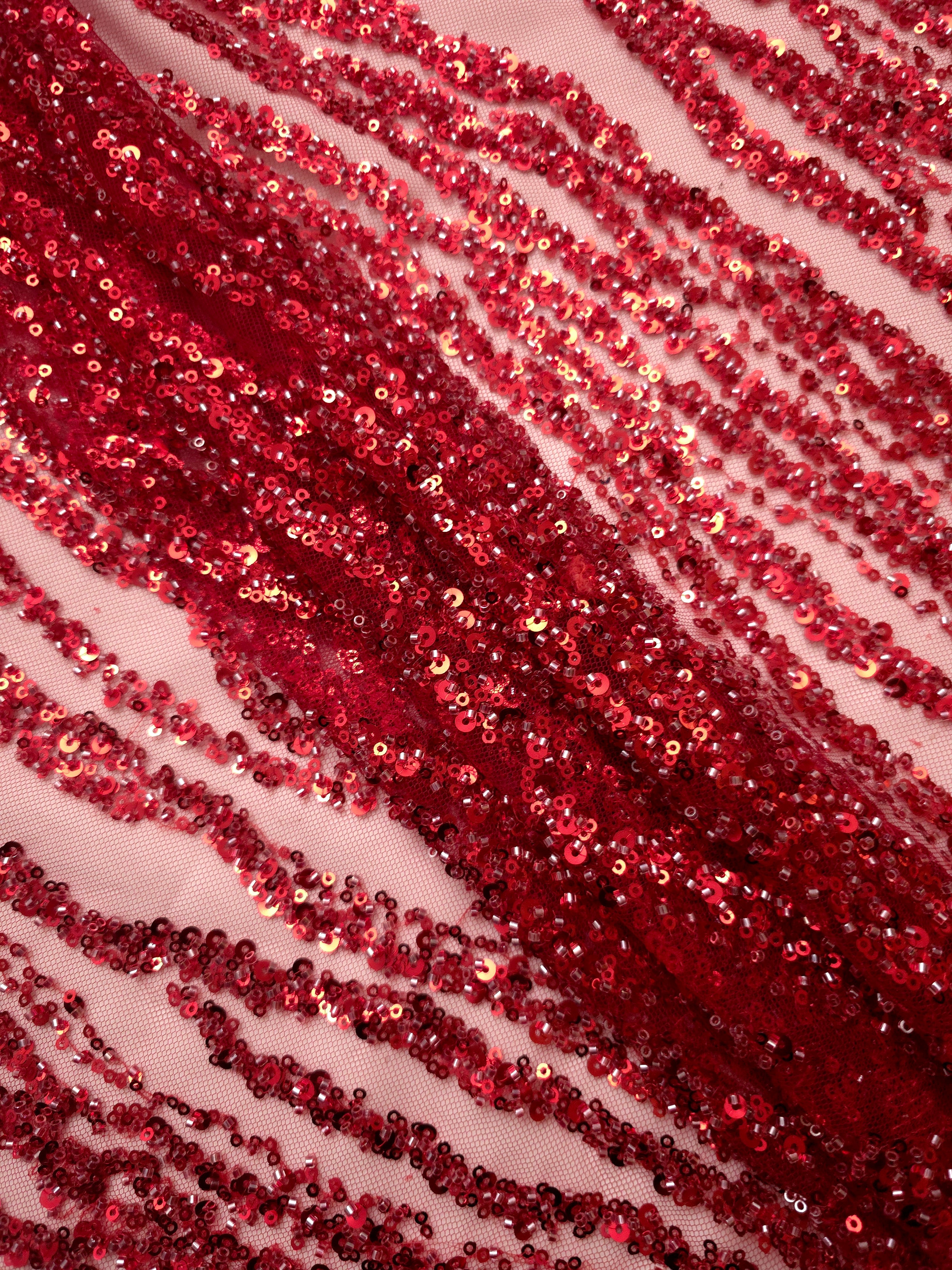 Extreme close-up of ruby red raised beadwork and sequin stitches forming the Zebra Strata textured pattern.