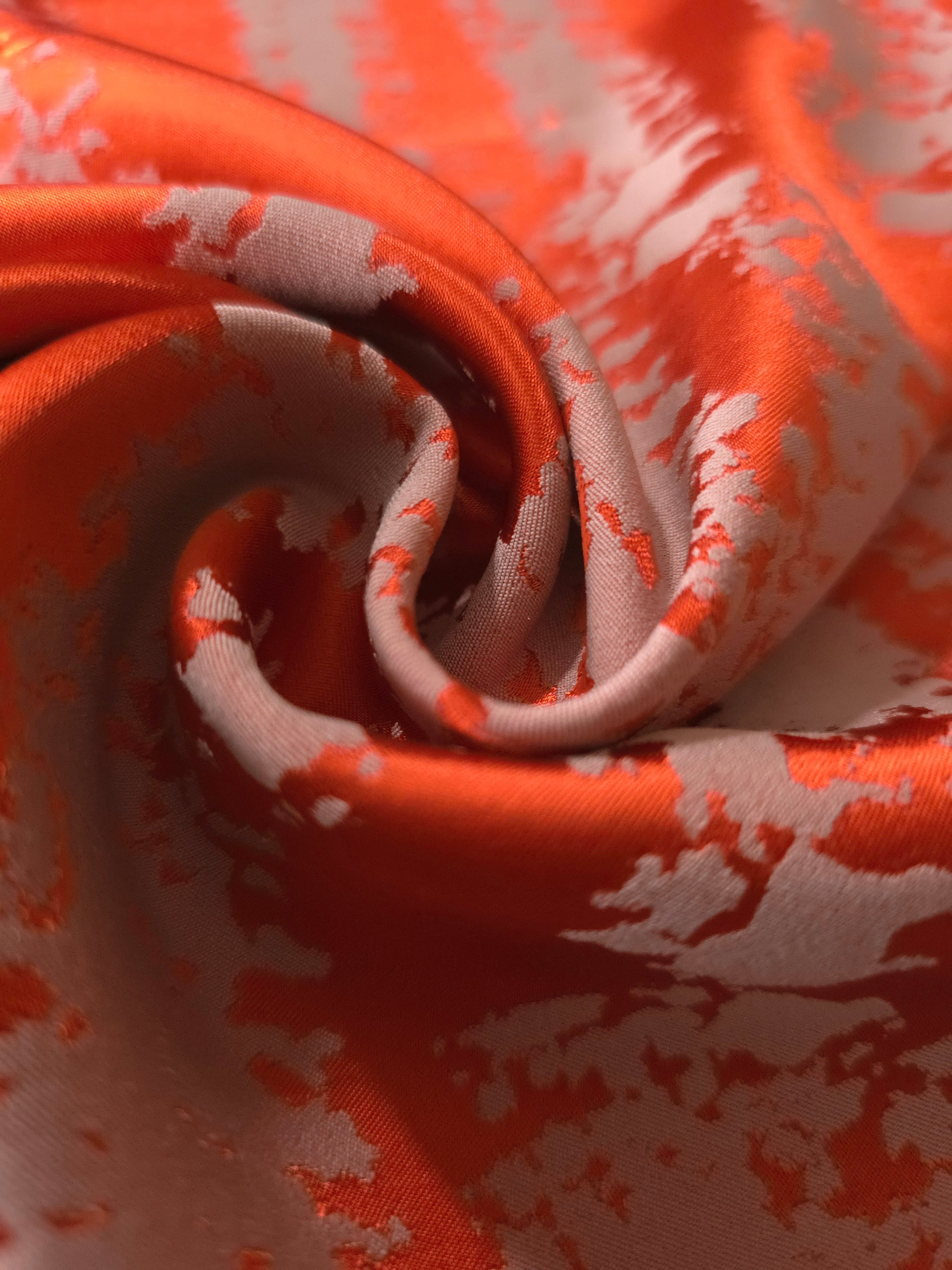A tight fold in the burnt orange satin, the grey-mauve patches breaking sharply at the crease
