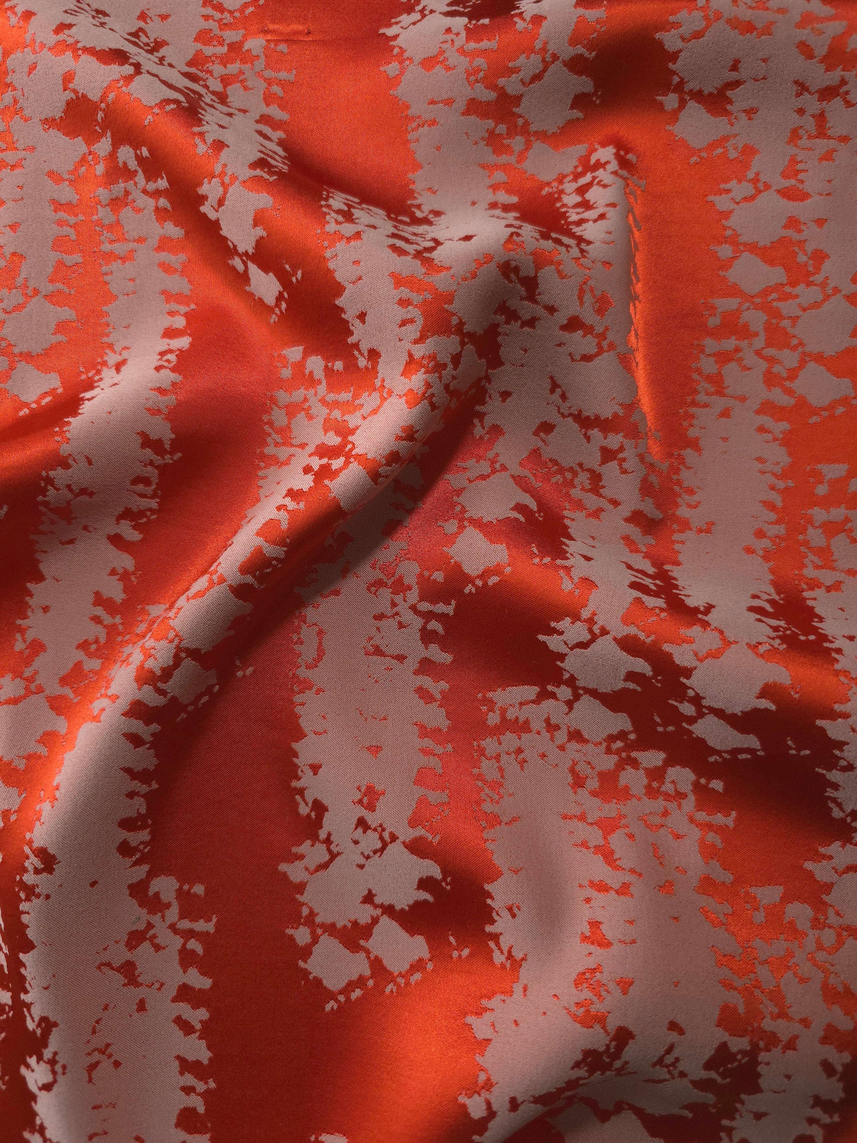 Burnt orange satin folded over, the grey-mauve mottled pattern standing out sharply against the bold base