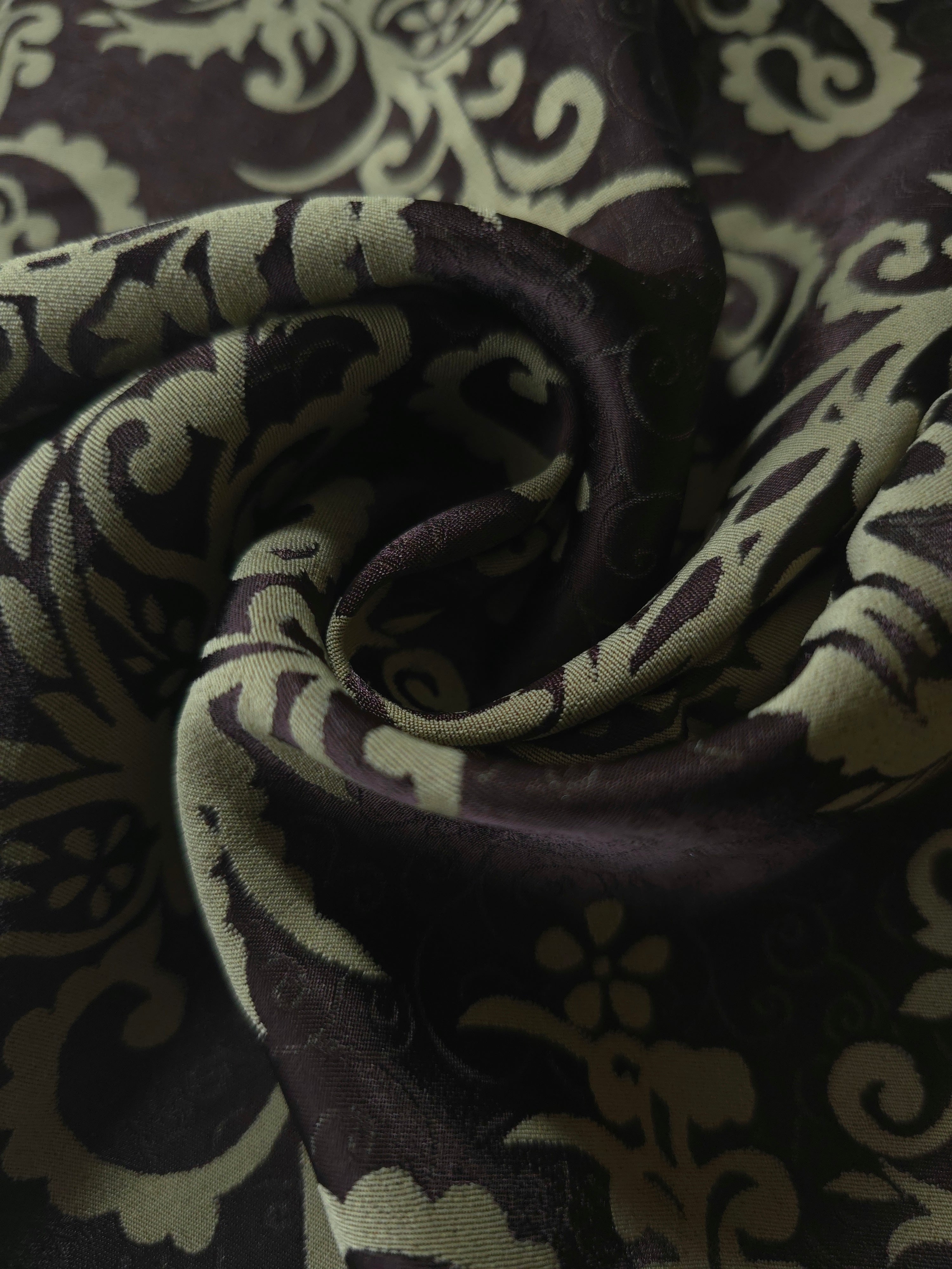 A tight fold in the brown satin, the baroque scrollwork bending sharply at the crease