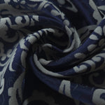 A tight fold in the navy satin, the grey scrollwork bending sharply at the crease