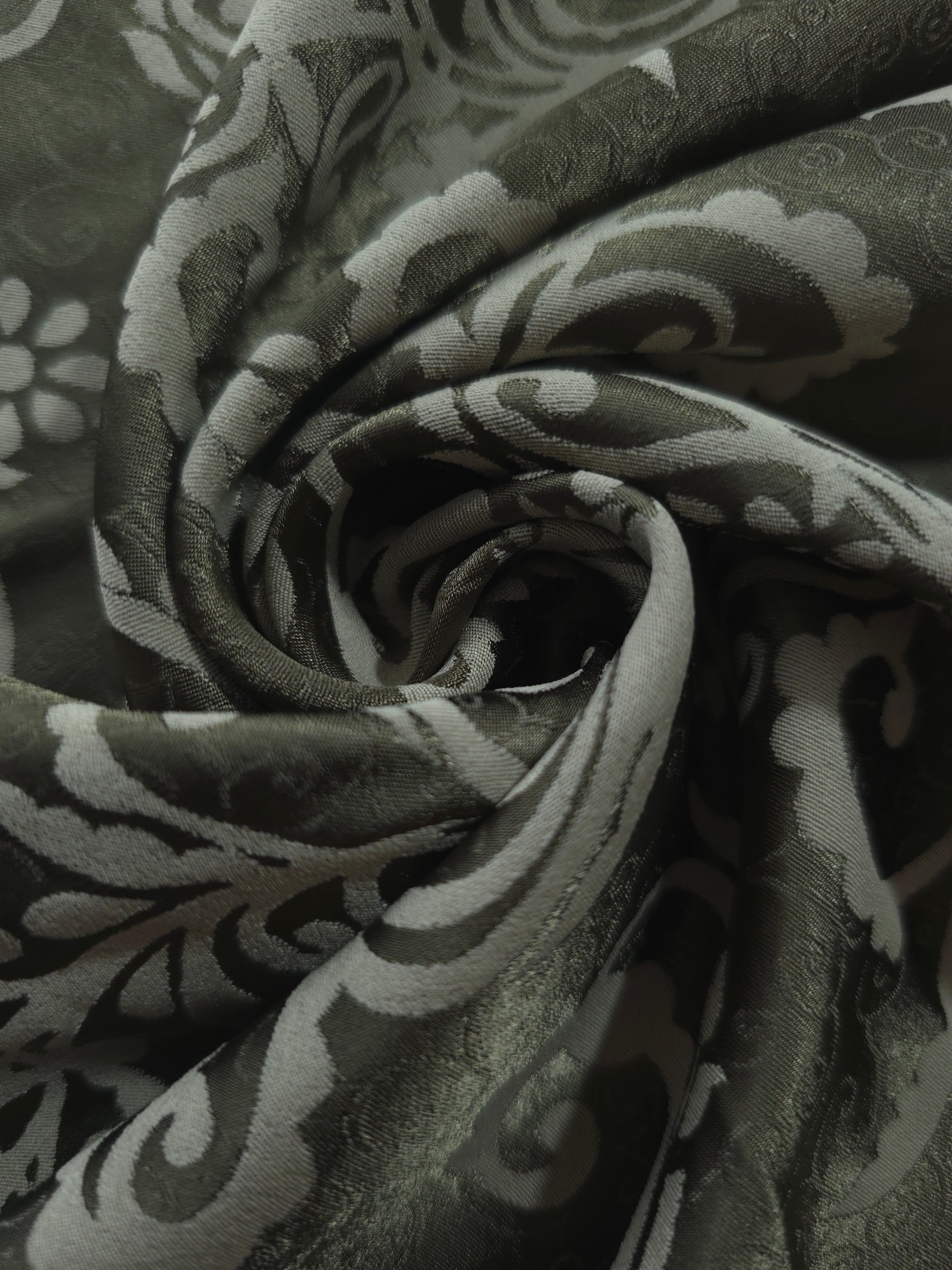A soft crease in the olive satin, the scrollwork only emerging where the light catches the surface