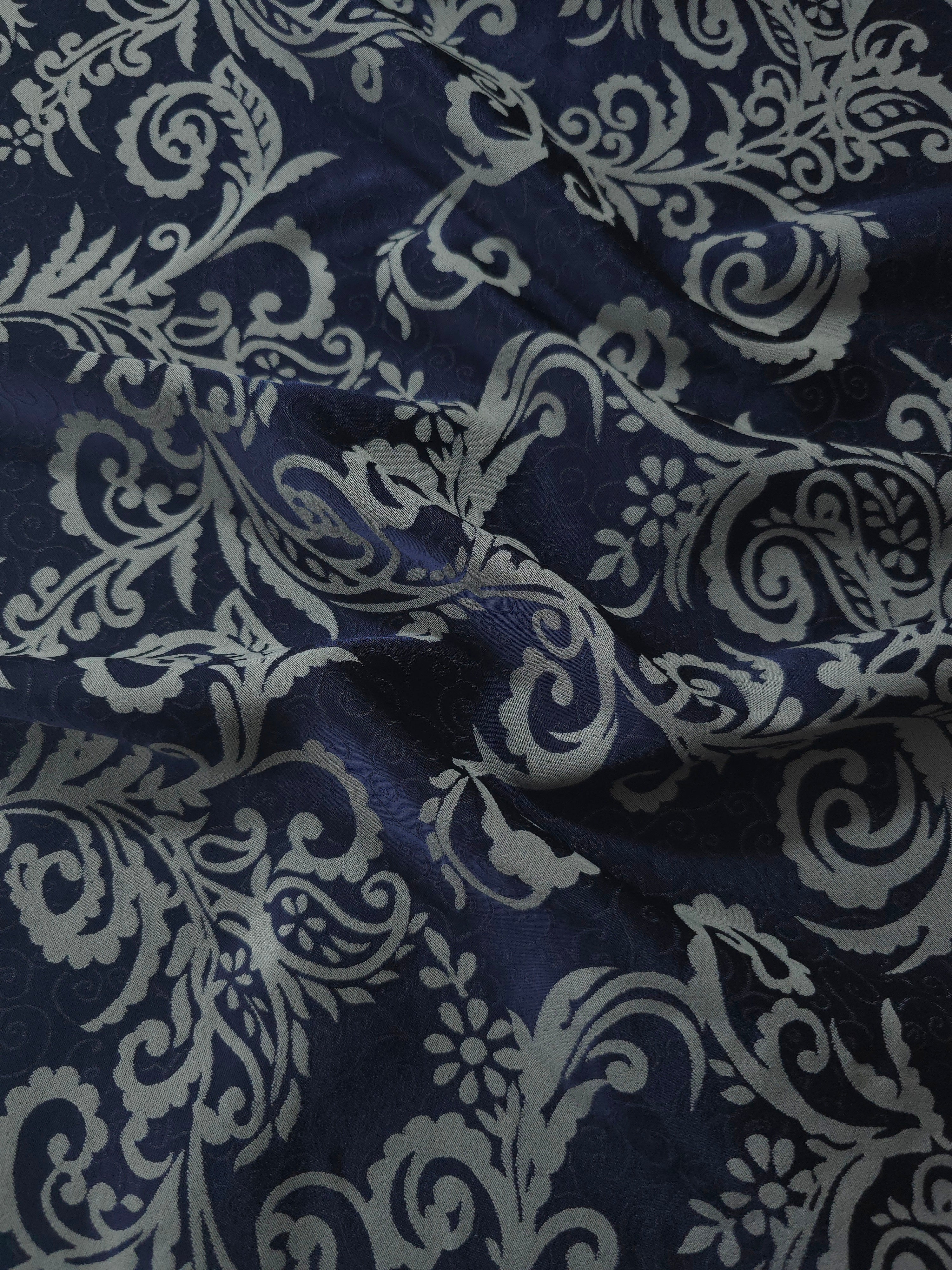 Navy satin folded over, the cool grey baroque scrollwork standing out crisply against the deep blue base