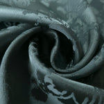 A soft crease in the teal satin, the floral spray only emerging where the light catches the surface