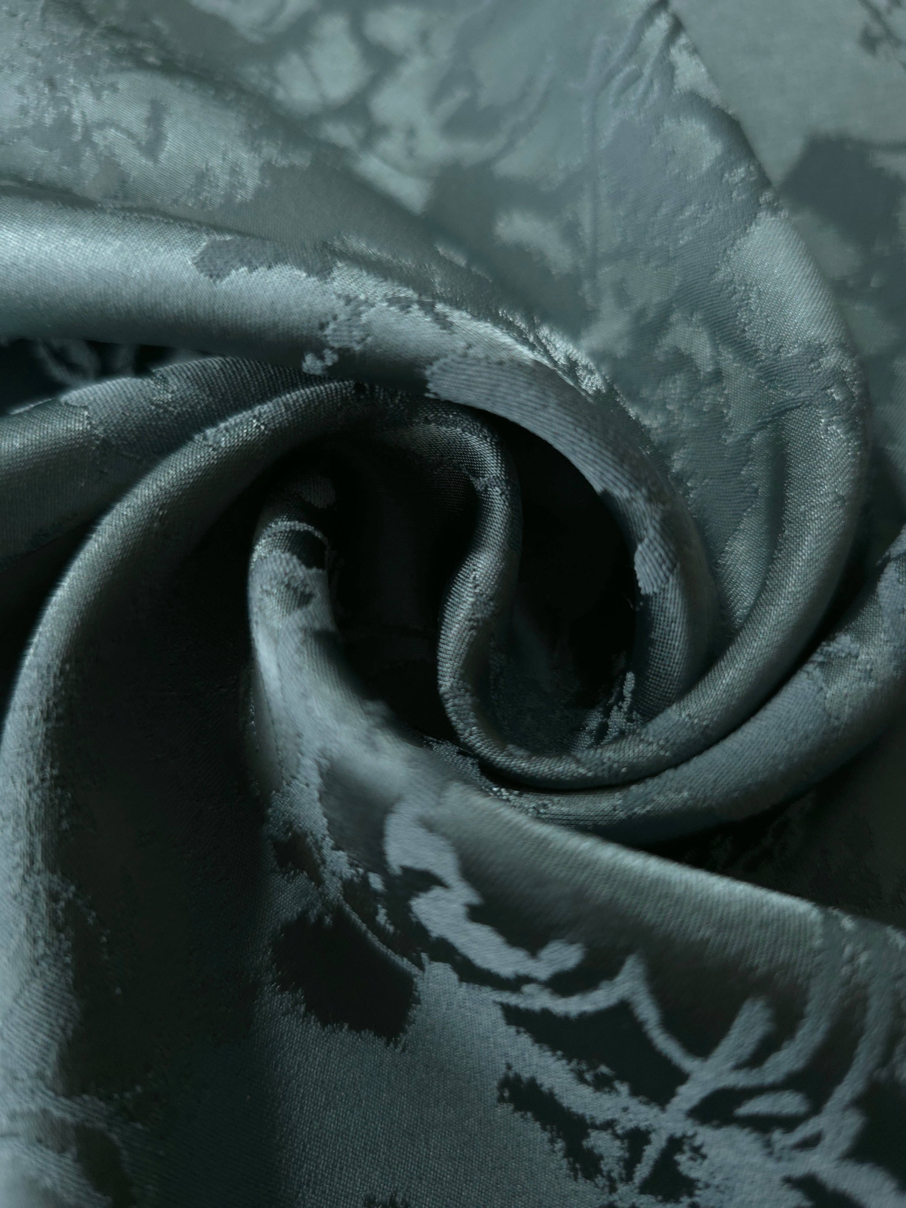 A soft crease in the teal satin, the floral spray only emerging where the light catches the surface