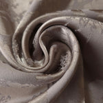 A gentle fold in the taupe satin, the floral spray catching light unevenly across the crease