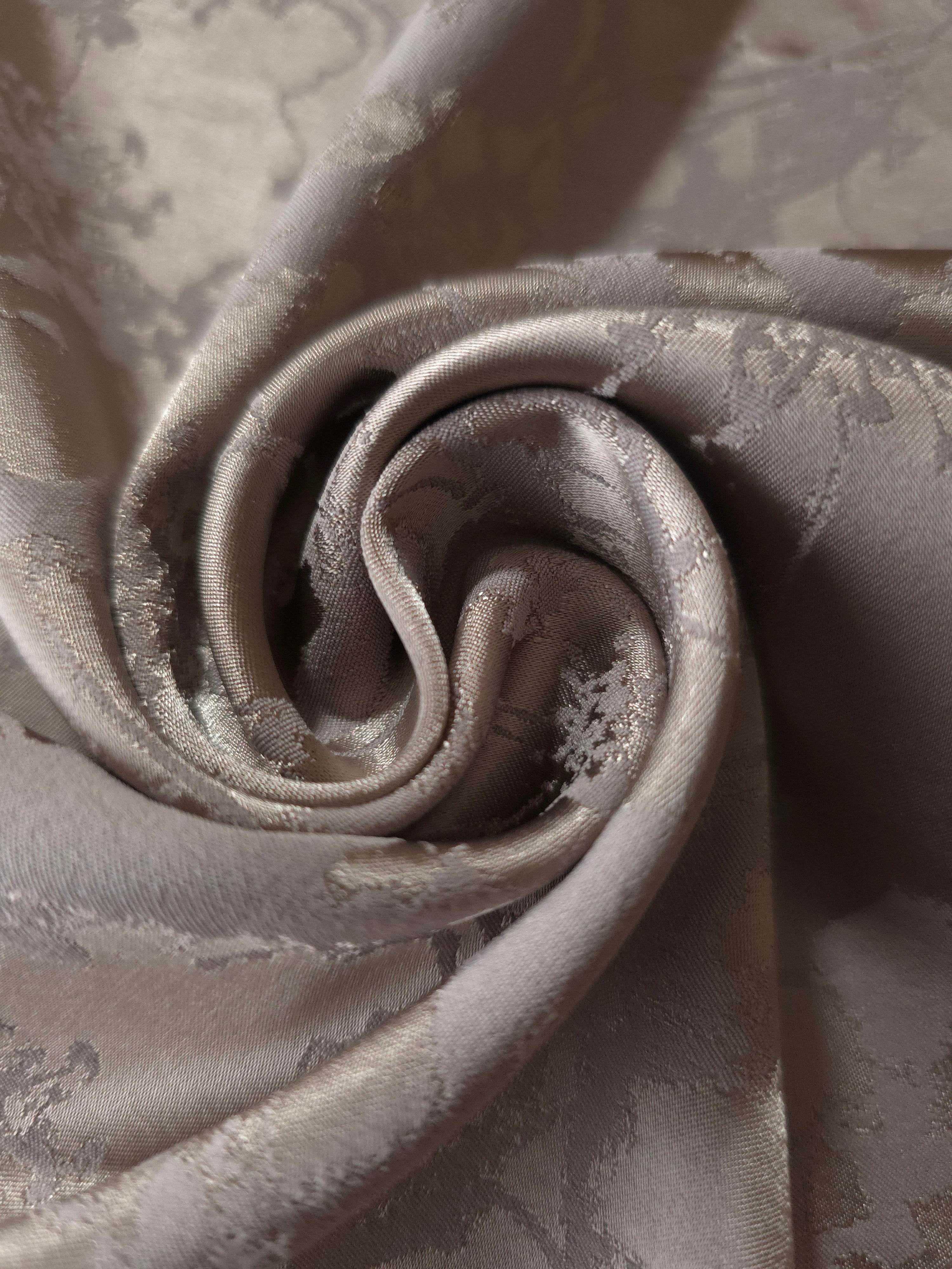 A gentle fold in the taupe satin, the floral spray catching light unevenly across the crease