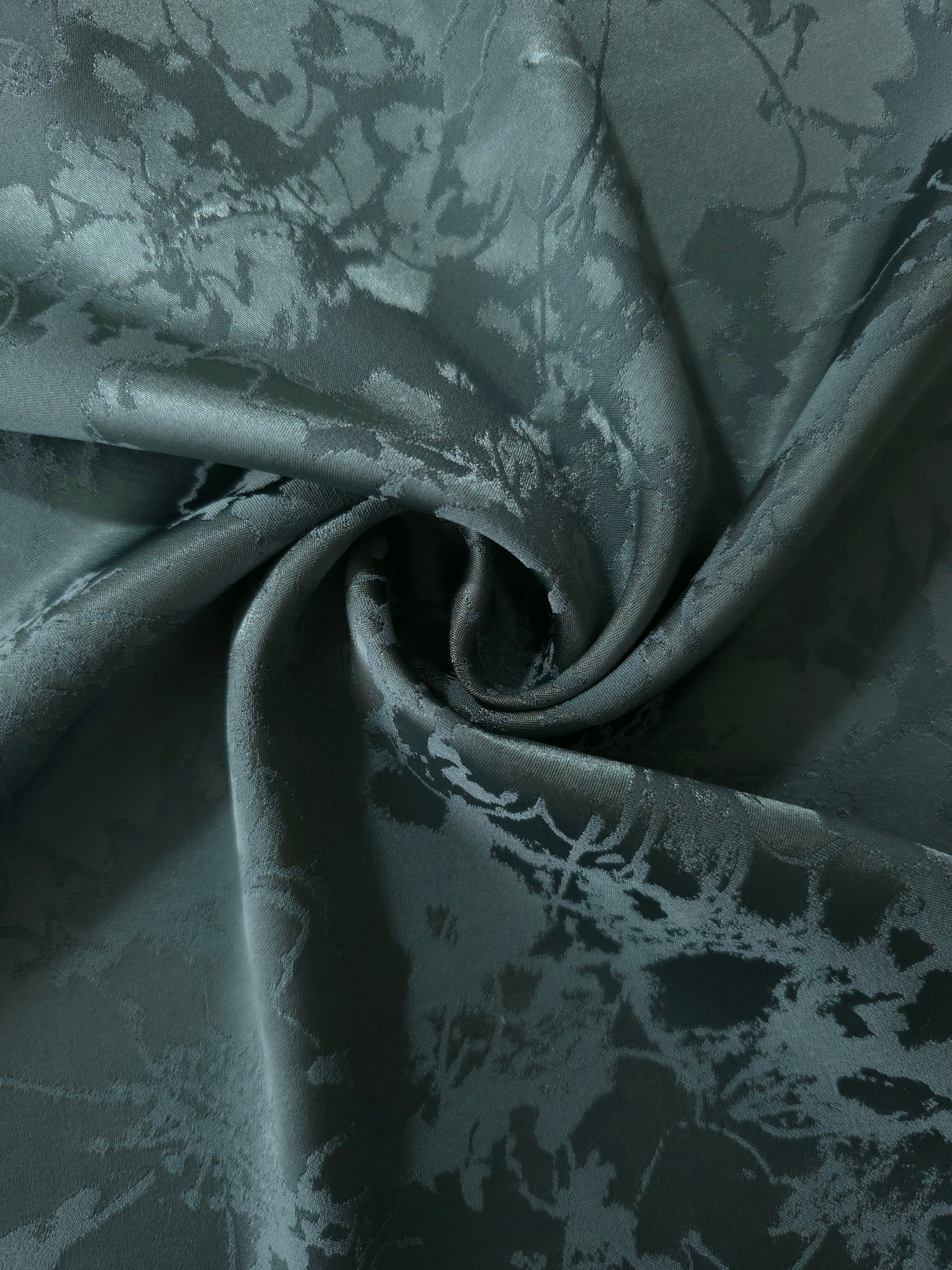 Teal floral satin draped in loose waves, the delicate tonal motif visible across the moving fabric
