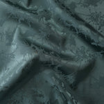 Deep teal satin folded over, the delicate botanical spray pattern reading almost entirely through tonal sheen
