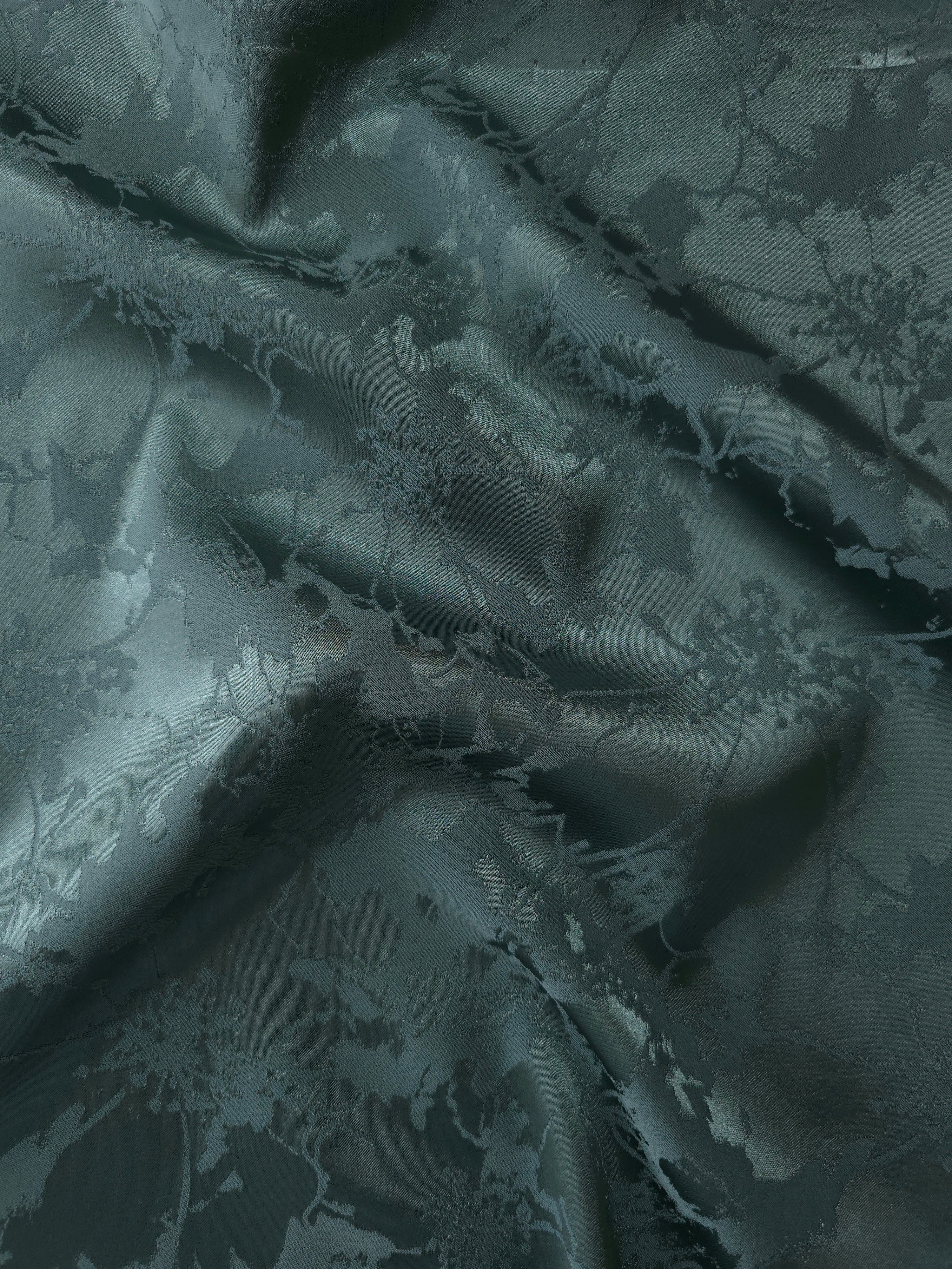 Deep teal satin folded over, the delicate botanical spray pattern reading almost entirely through tonal sheen