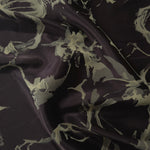 Black satin folded over, the sage-olive abstract splatter motif breaking unevenly across the dark base