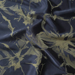 Navy-charcoal satin folded over, the olive-tan splatter motif standing out against the dark blue-grey base