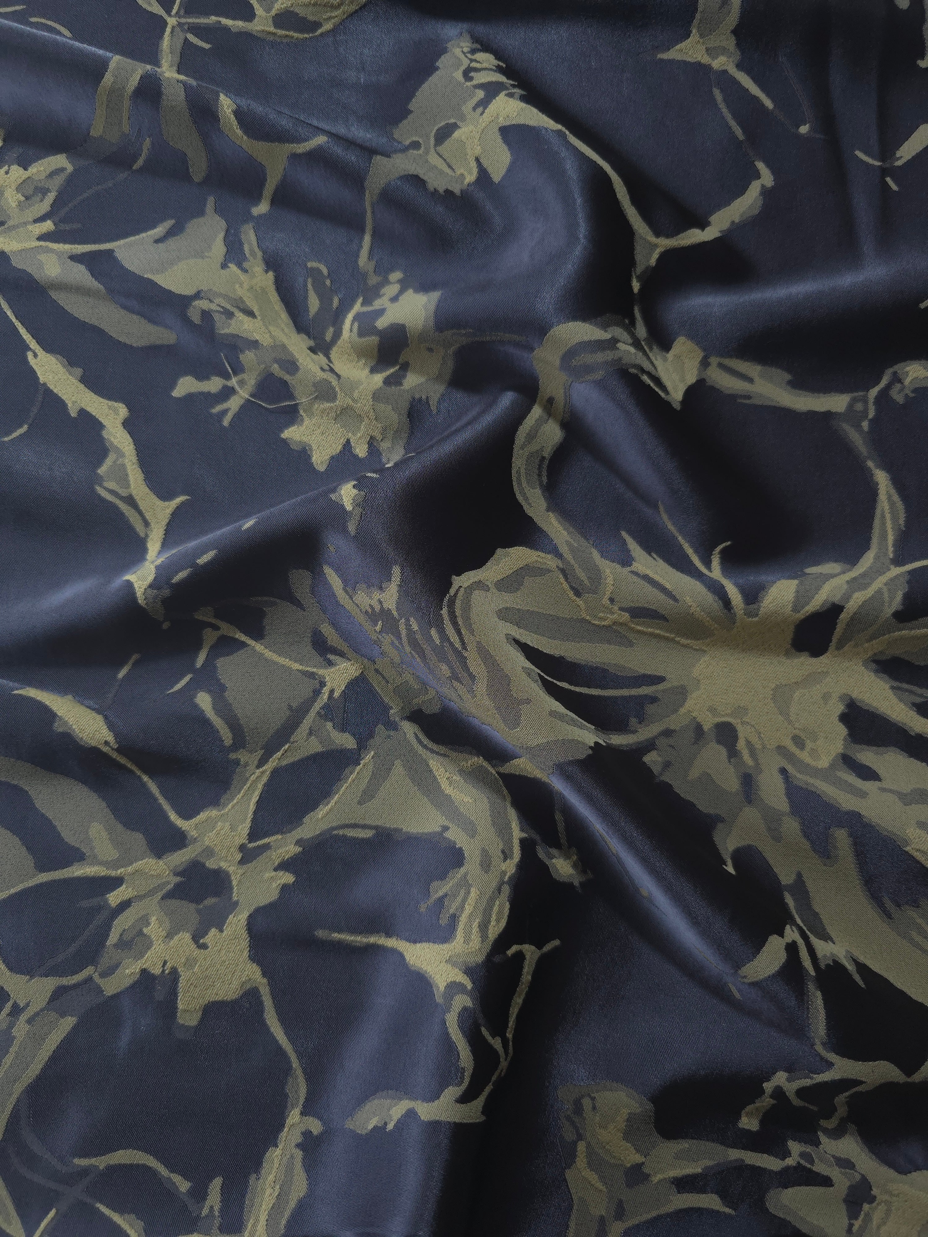 Navy-charcoal satin folded over, the olive-tan splatter motif standing out against the dark blue-grey base