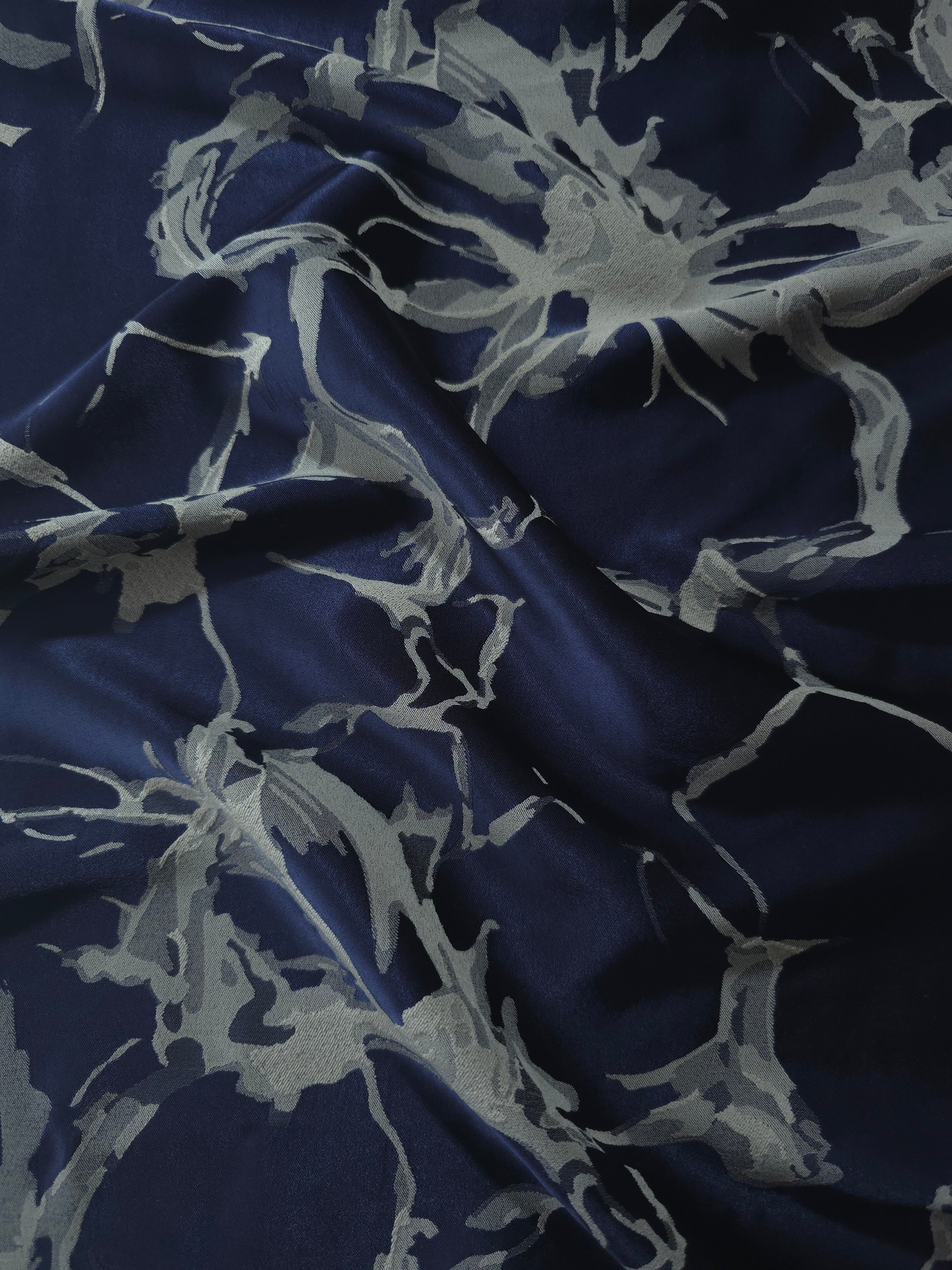Navy satin folded softly, the grey-blue fractured line motif reading as branching abstract shapes