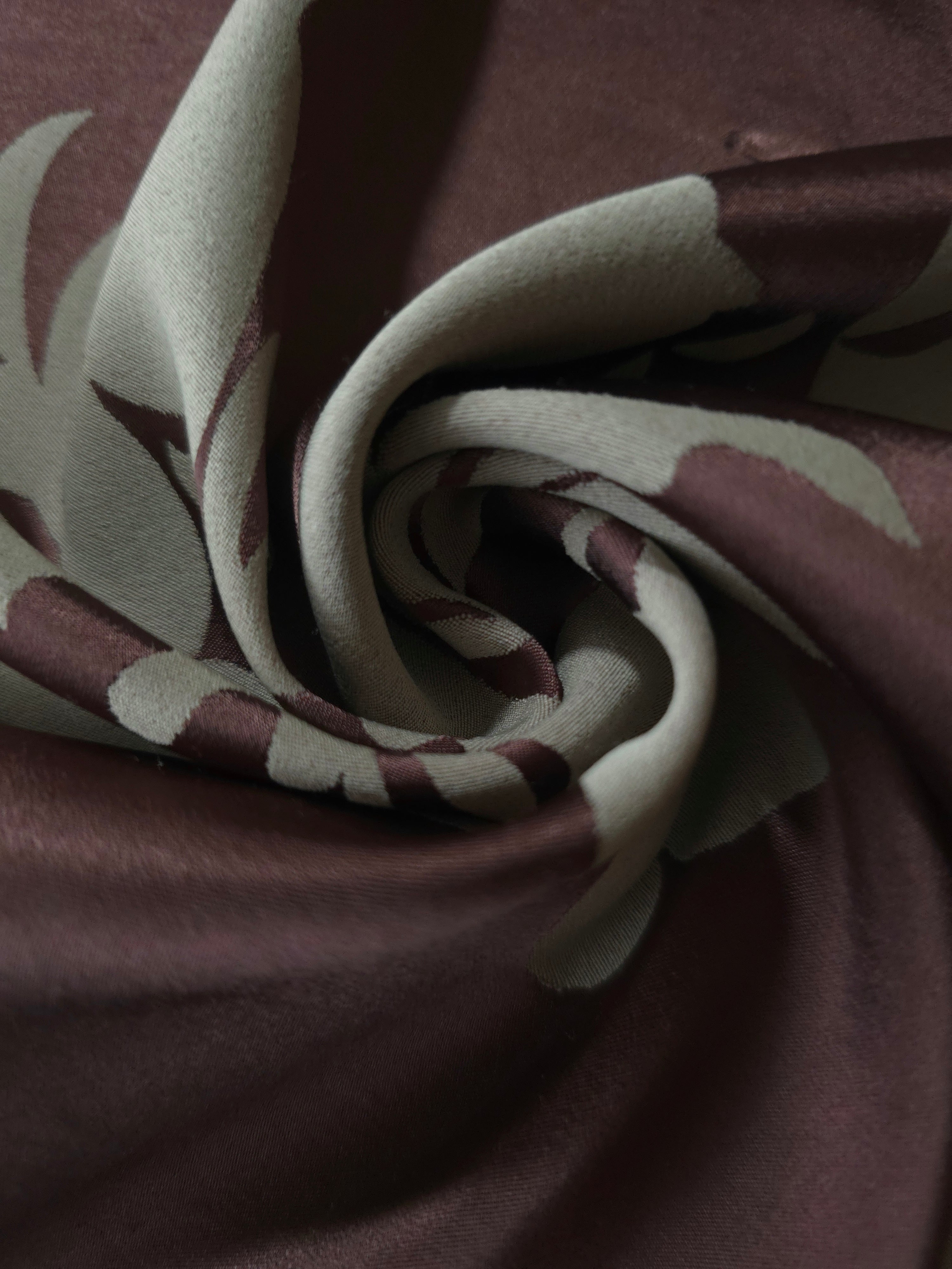 A tight fold in the wine satin, the hibiscus petal outline bending sharply at the crease