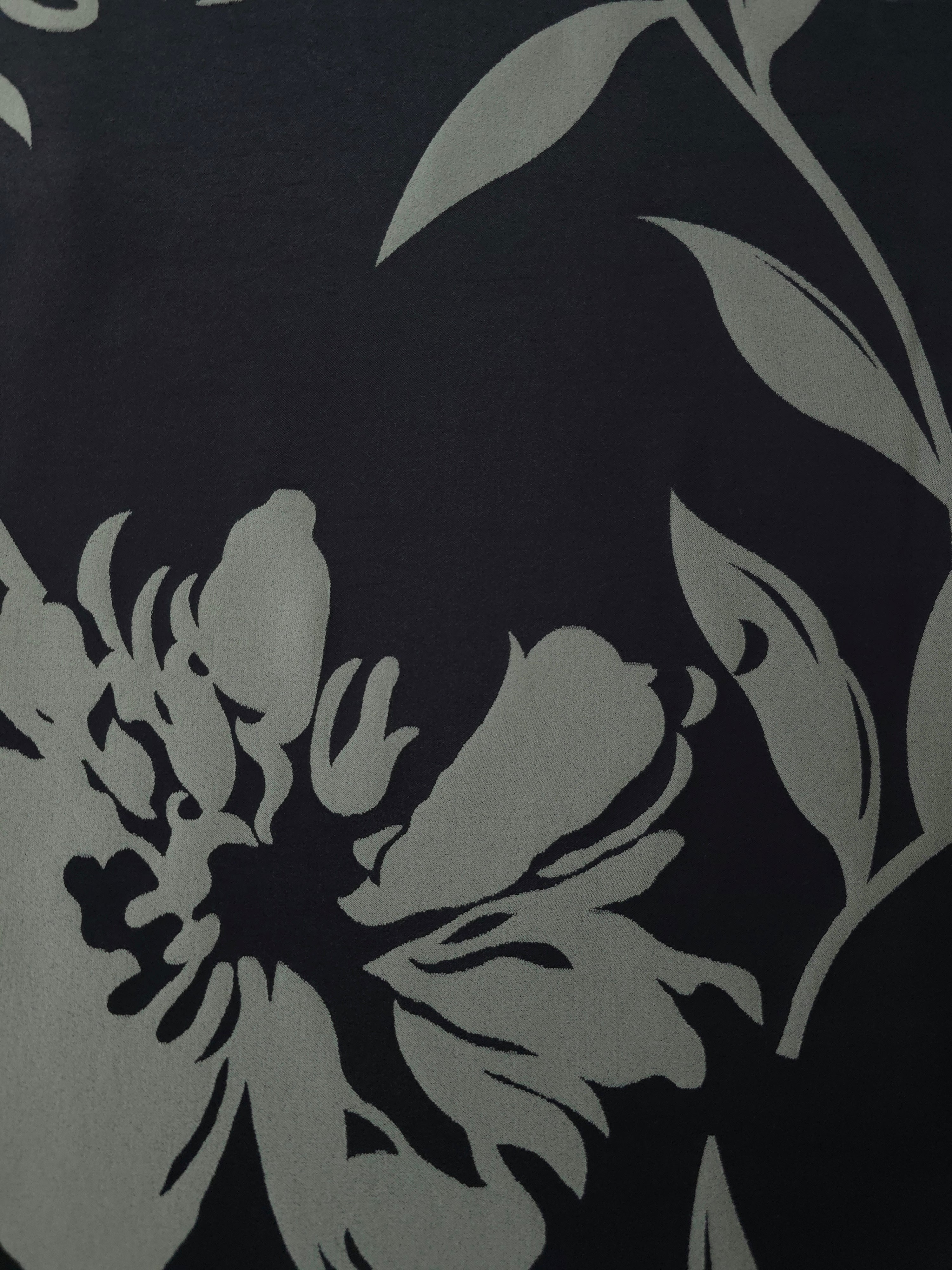 A wider view of the black and sage hibiscus satin laid flat, showing the full bloom repeat