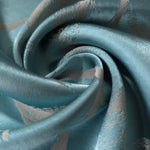 A tight fold in the teal satin, the leaf branches bending visibly at the crease