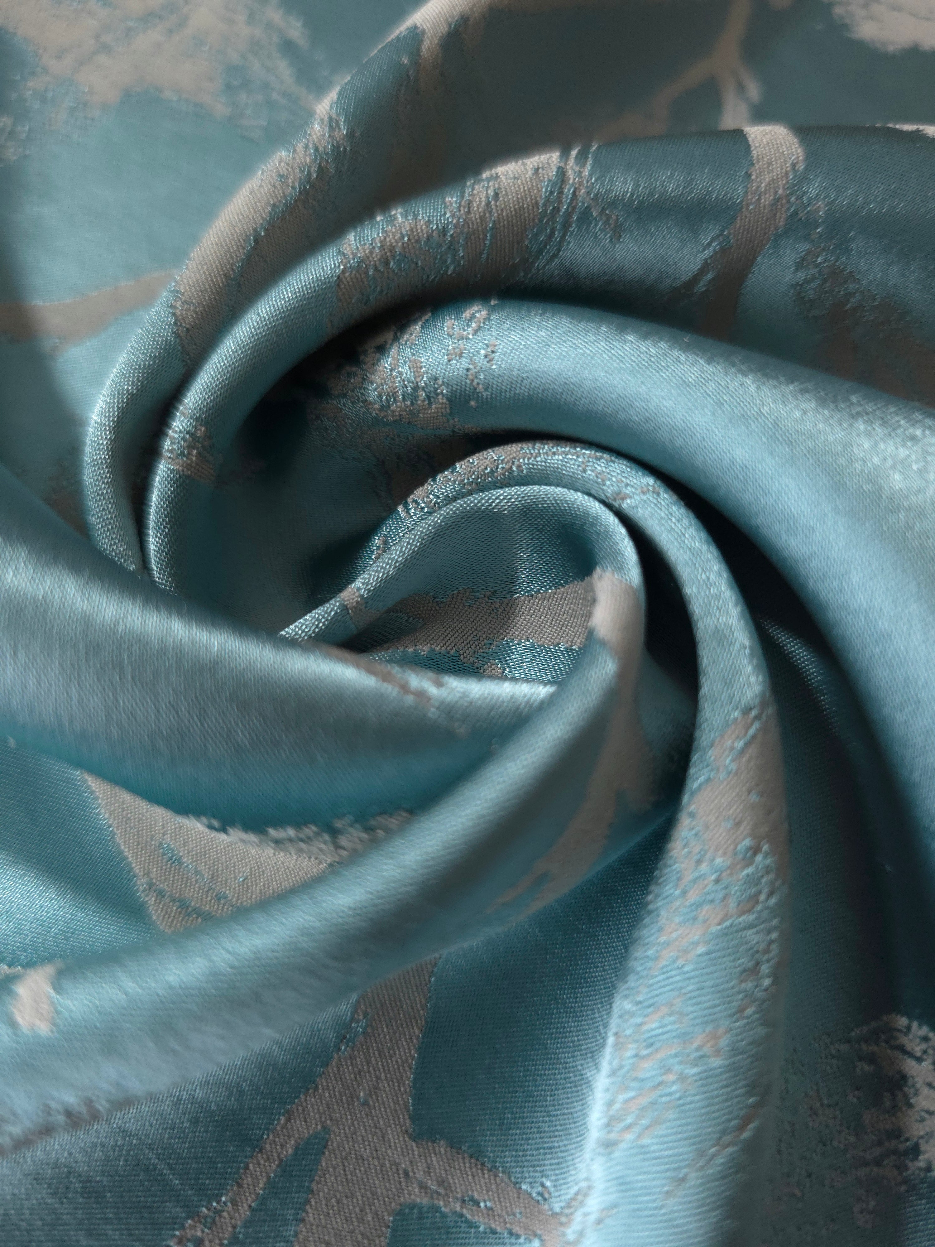A tight fold in the teal satin, the leaf branches bending visibly at the crease