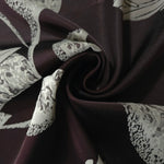 Plum lily flower satin draped to catch the light, the textured petal fill visible across the fold