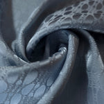A tight fold in the slate blue satin, the lattice rows bending in step with the crease