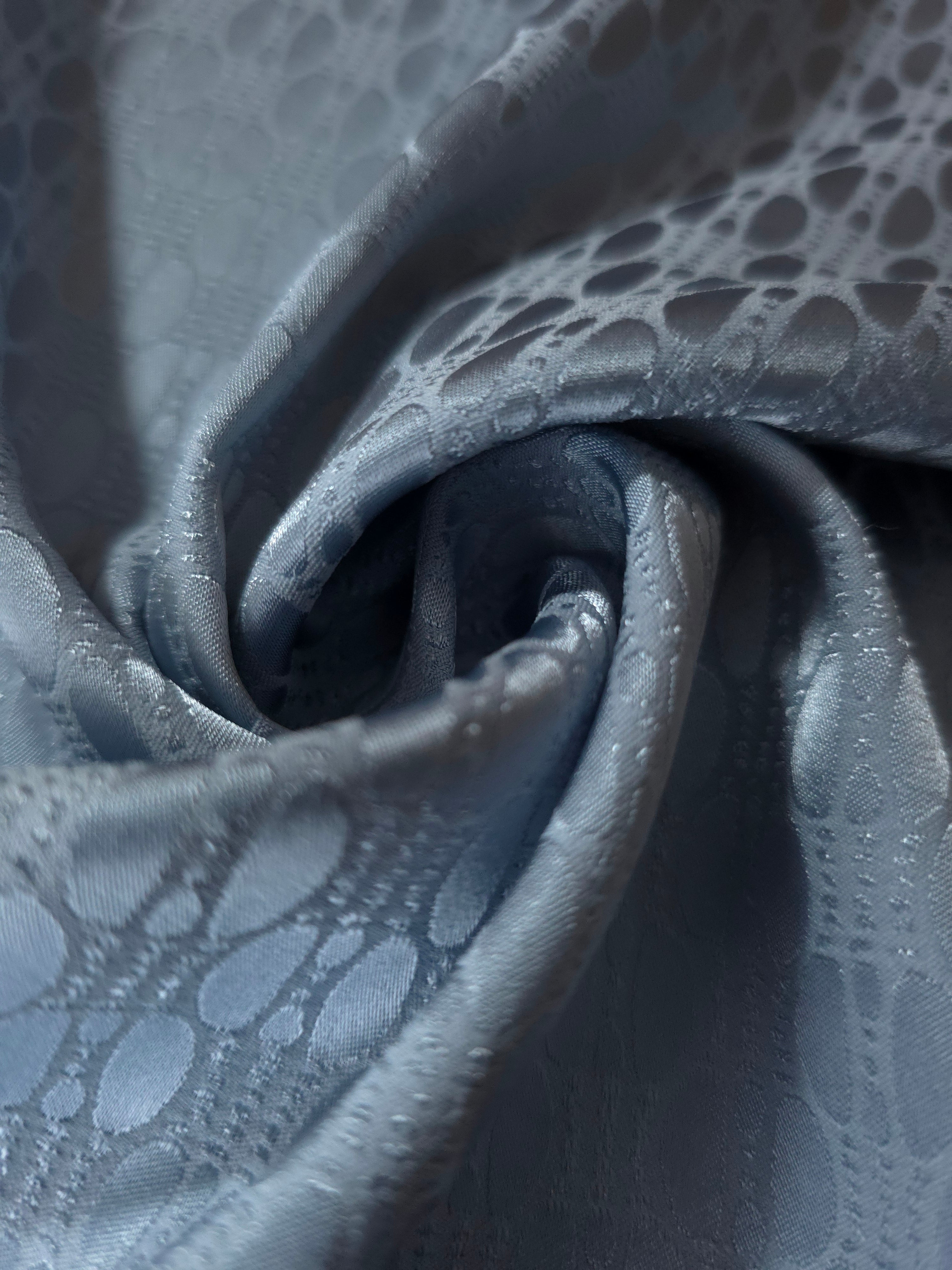 A tight fold in the slate blue satin, the lattice rows bending in step with the crease