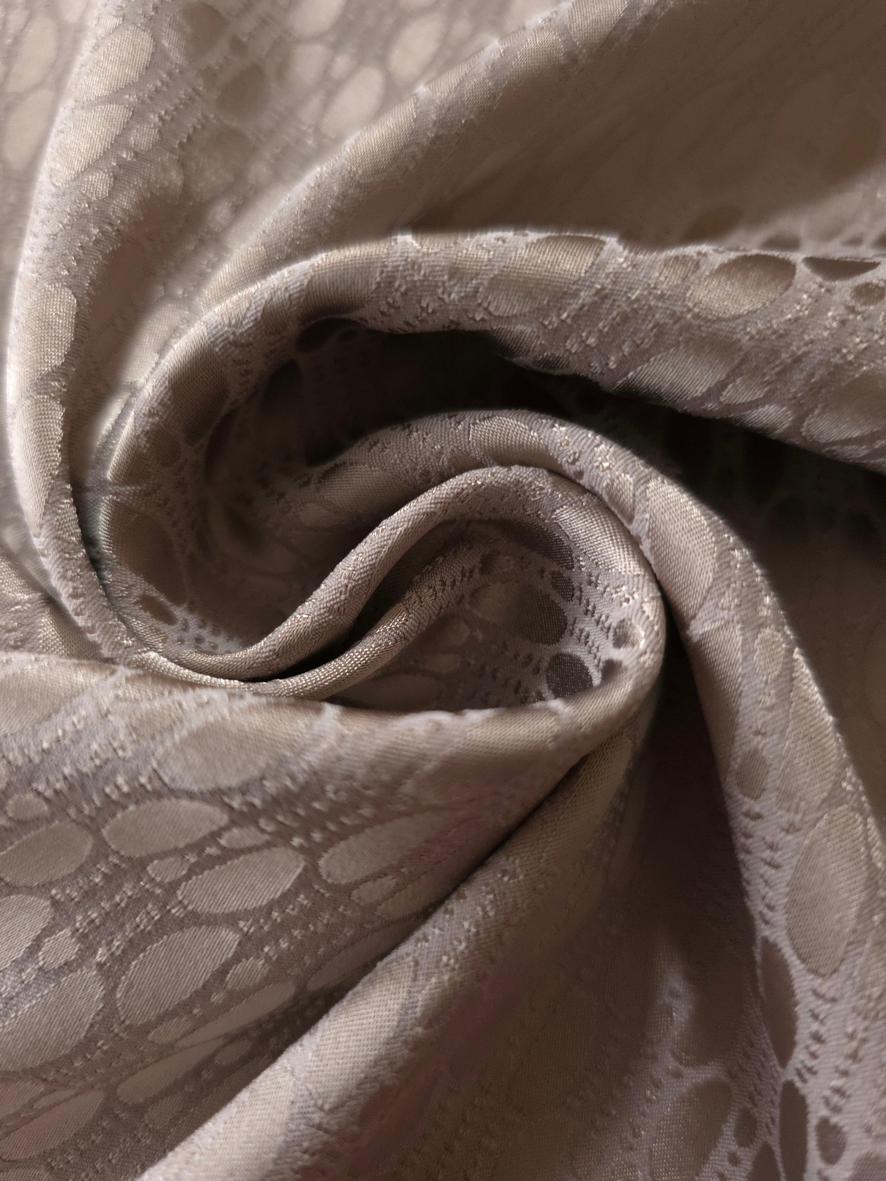 A soft crease in the taupe-bronze satin, the lattice rows catching light unevenly at the fold