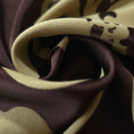 A tight fold in the aubergine satin, the sage flower outline bending sharply at the crease