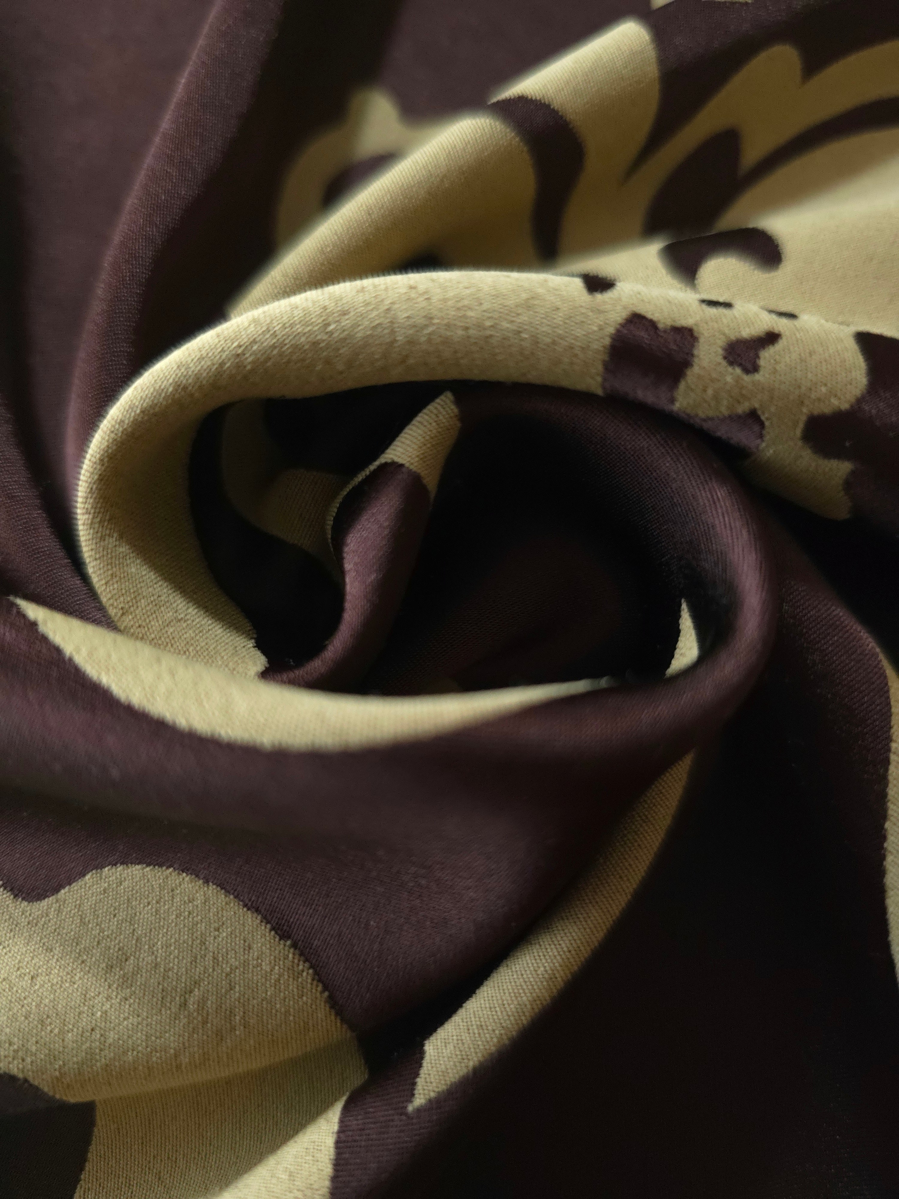 A tight fold in the aubergine satin, the sage flower outline bending sharply at the crease