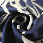 A tight fold in the navy satin, the silver flower silhouette bending visibly at the crease