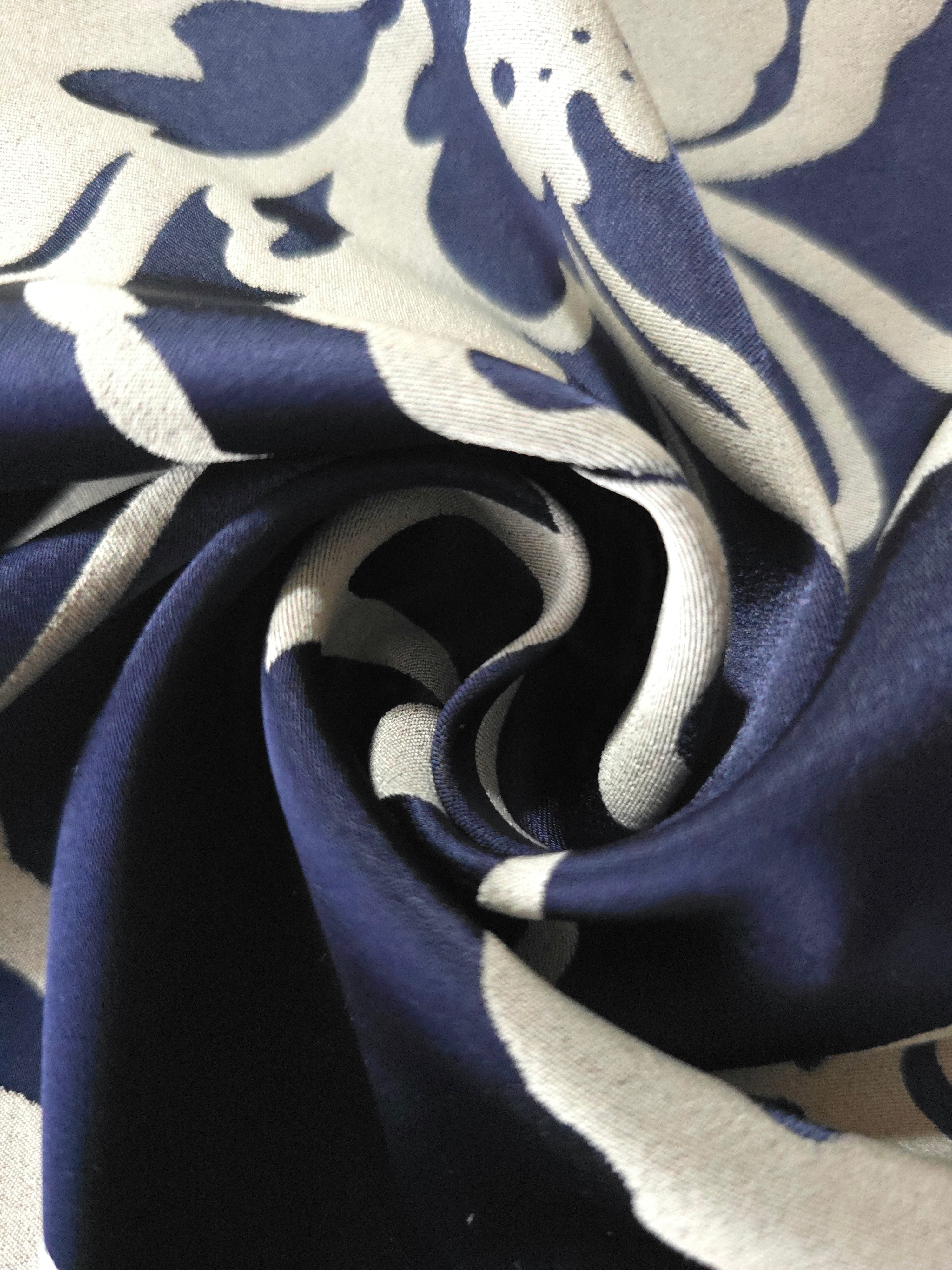 A tight fold in the navy satin, the silver flower silhouette bending visibly at the crease